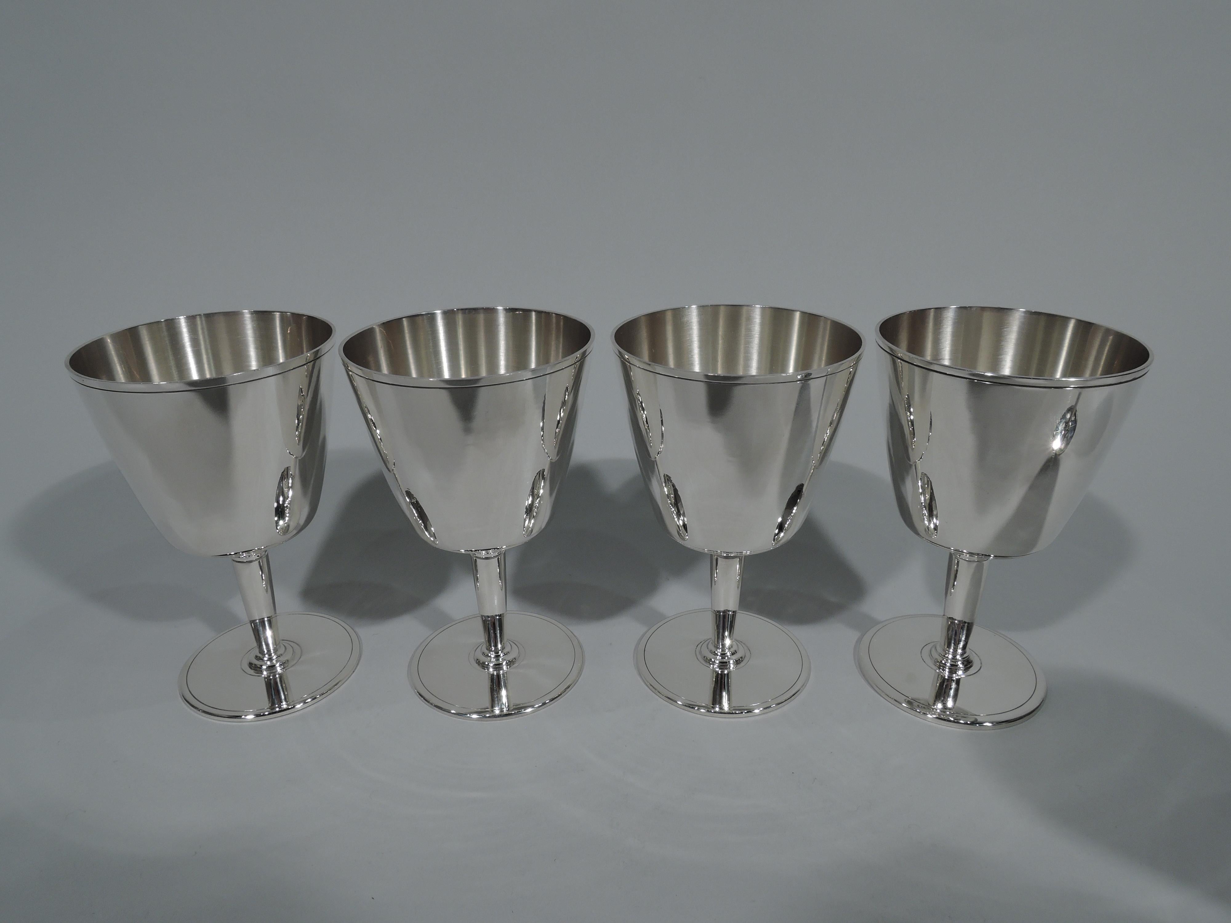 Set of 12 Art Deco sterling silver cocktail cups. Made by Tiffany & Co. in New York. Each: Truncated cone with flat bottom, tapering stem, and flat circular foot. Incised bands on bowl rim and foot rim. Spare and functional. Hallmarks include