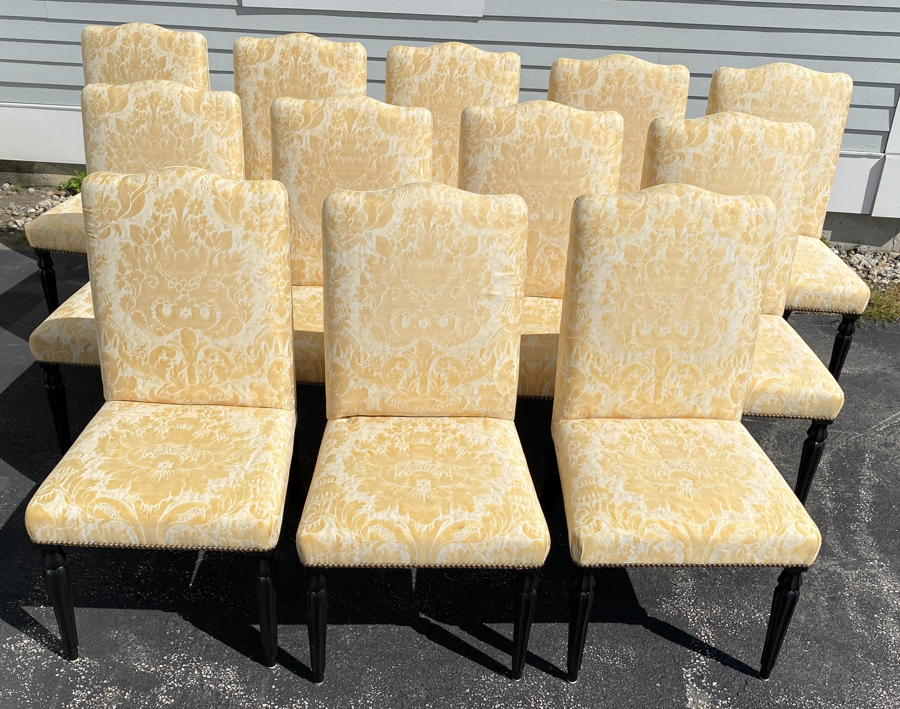 A fine set of 12 dining chairs with Fortuny style floral yellow upholstery, arched crests, and black fluted turned legs. The set is in very good overall condition, with some minimal spot stains, some minor wiggle on several of the chairs, minor leg