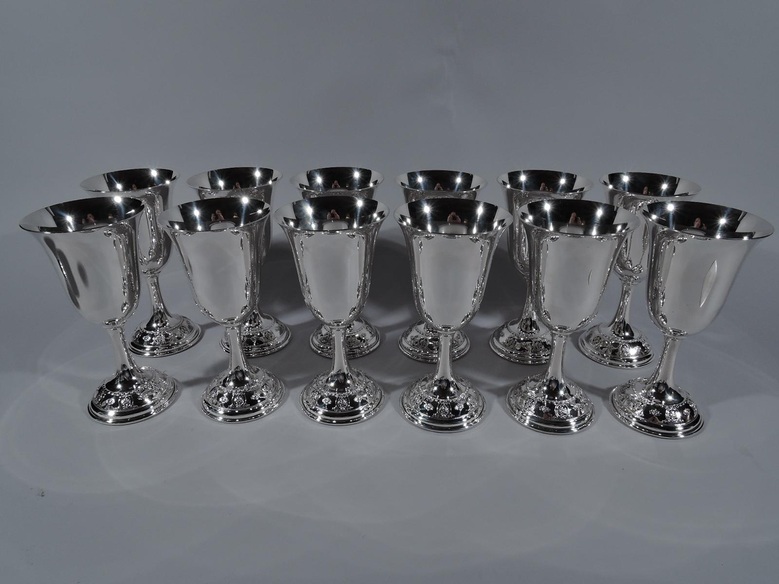 Set of 12 rose point sterling silver goblets. Made by Wallace in Wallingford, Conn. Each: Tapering bowl with fluted rim, cylindrical stem, and raised foot. Foot has chased flower heads alternating with open scrolled ovals inset with flowers. Fully