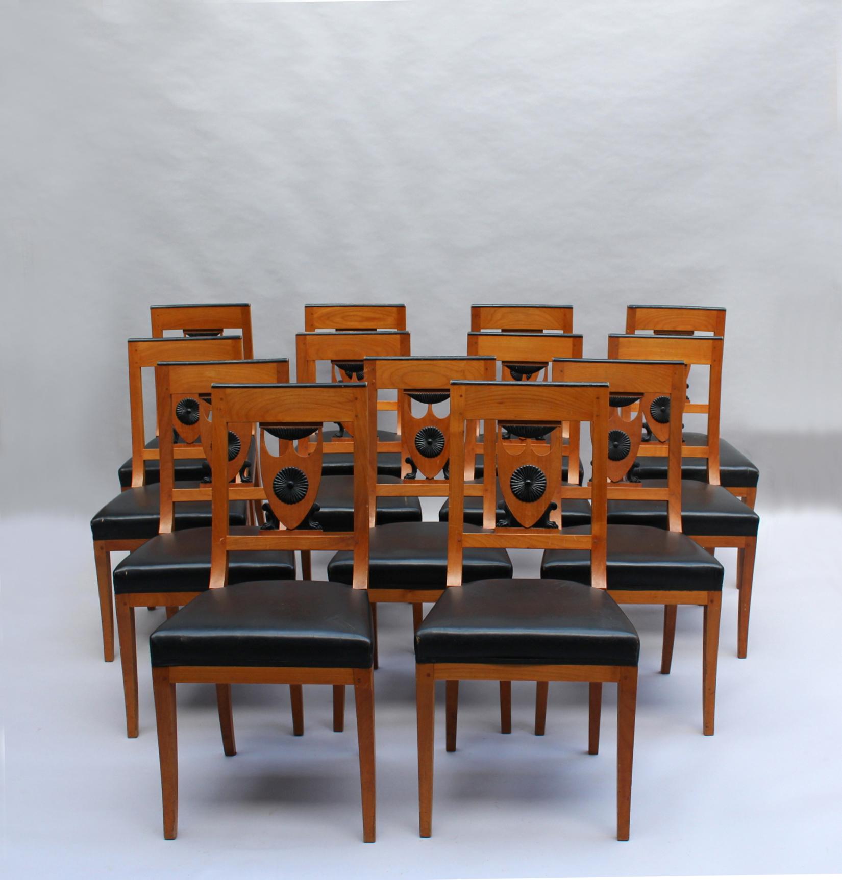Satz von 13 feinen französischen neoklassischen Kirschholz-Esszimmerstühlen im Empire-Directoire-Stil mit geschnitzten und geschwärzten Holzdetails.