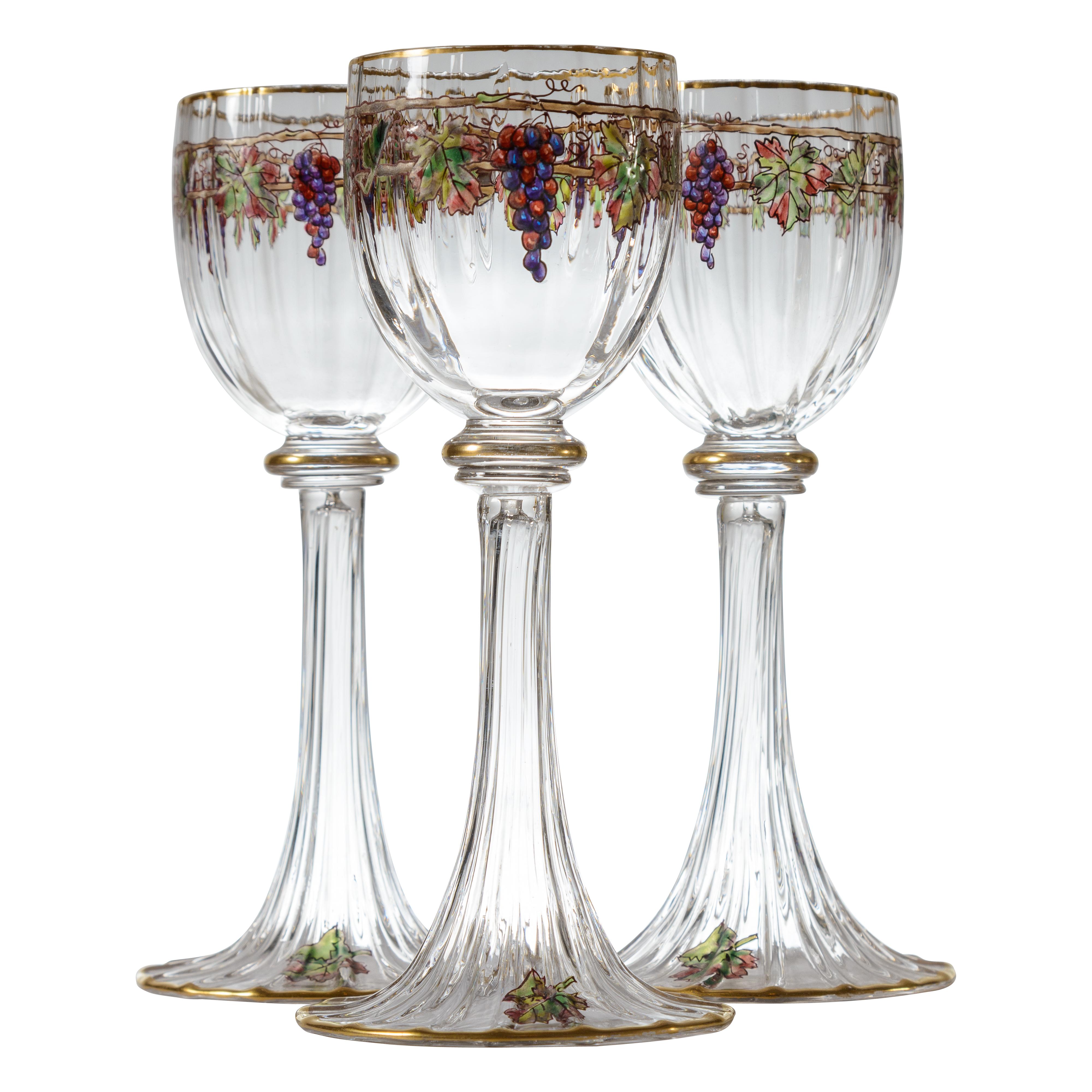 An elegant set of antique crystal wine glasses beautifully blown with an optic cut and trumpet form fluted bases. Hand enameled with purple and green grapes and vines. Trimmed on the cup, knob stem and base with 24 karat gold. Attributed to one of