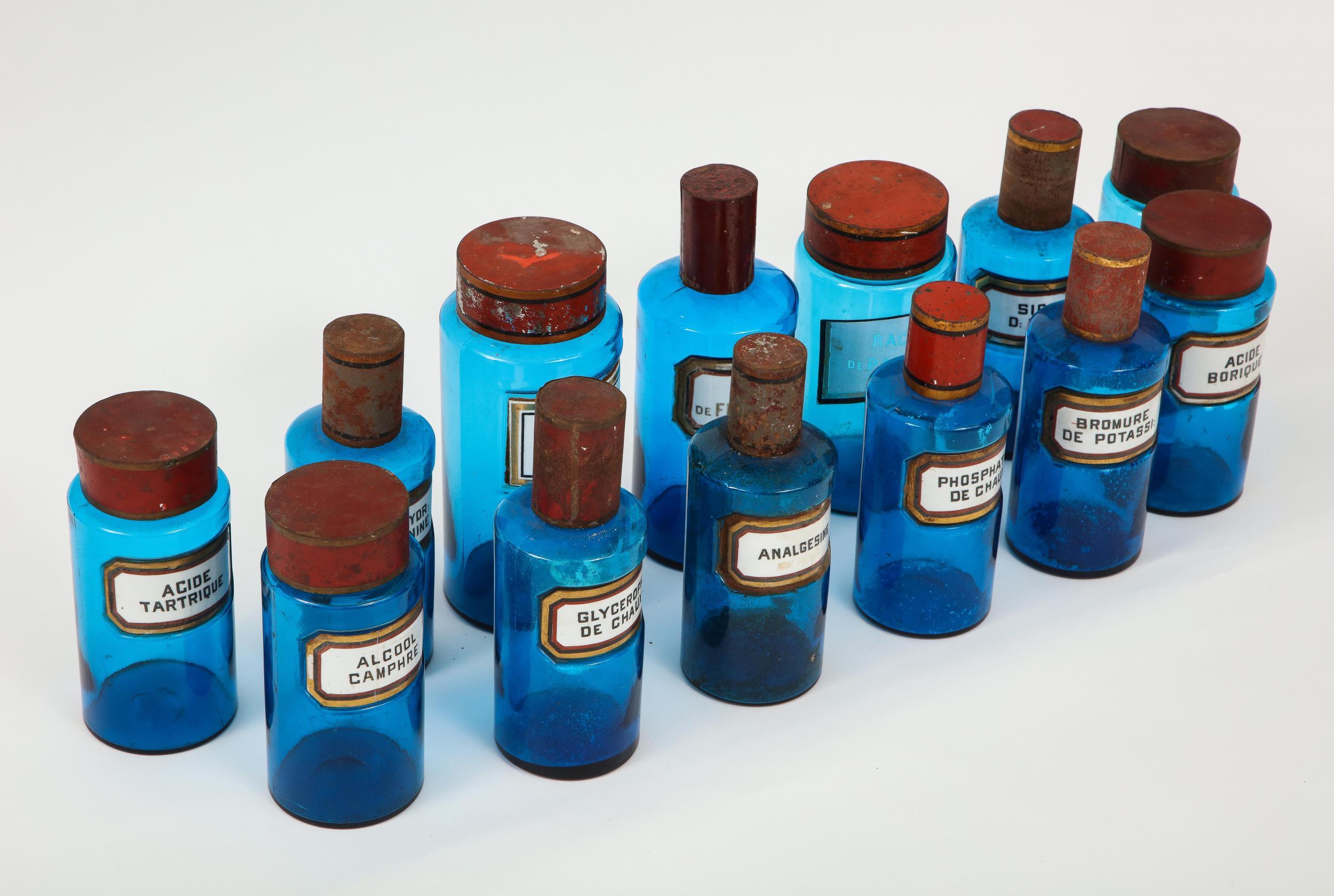 A stunning set of fourteen French apothecary or pharmacy jars. A clear and vibrant blue glass with white enameled labels and red metal caps. Bottle labels include linseed, boric acid, and lime phosphate. A great way to add color to bookshelves or