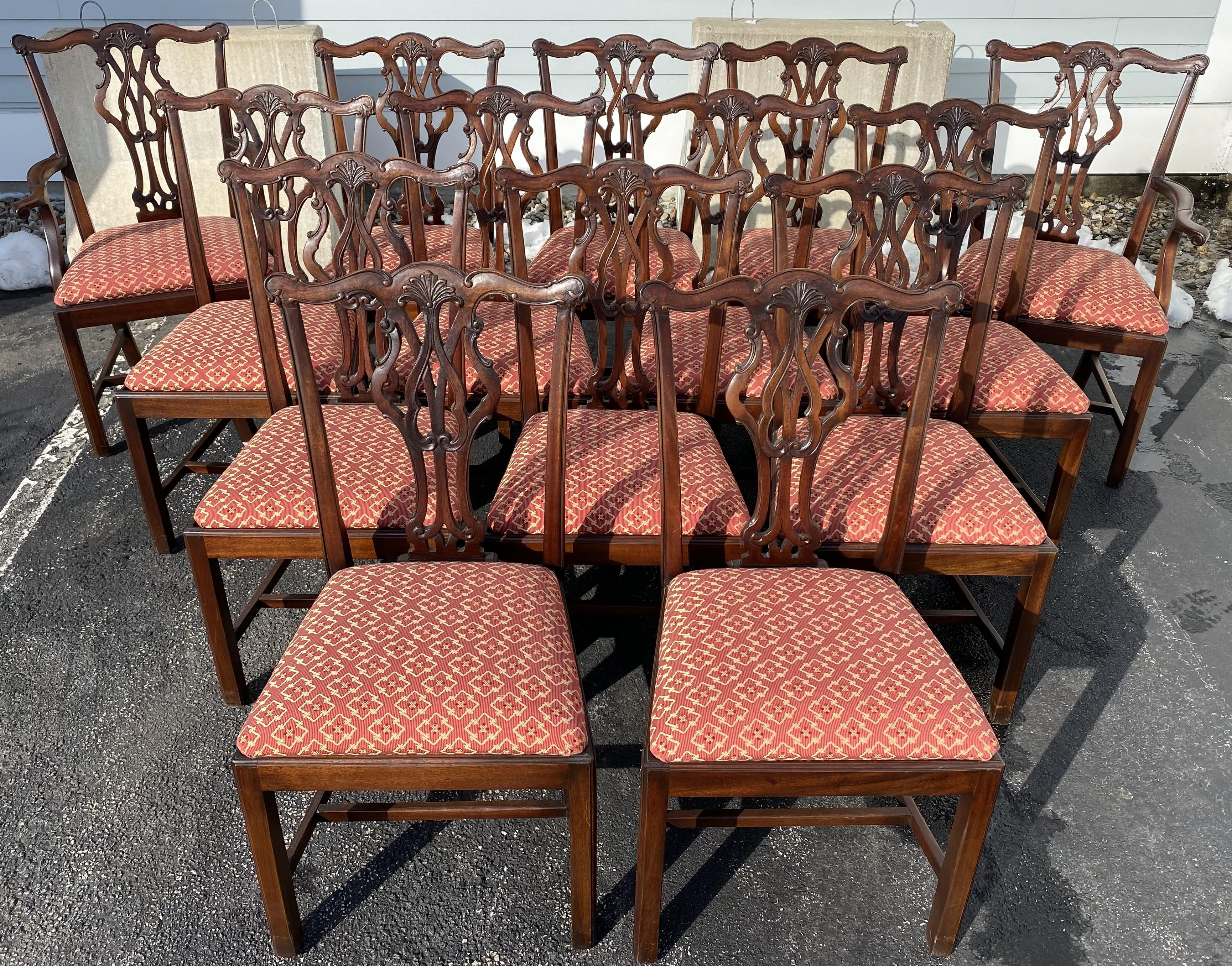 Un bellissimo set di 14 sedie da pranzo in mogano in stile Chippendale, tra cui due poltrone e 12 sedie laterali, ognuna con creste decorative ben intagliate e stecche intagliate a traforo, sedili imbottiti geometrici, braccioli a voluta e barelle a