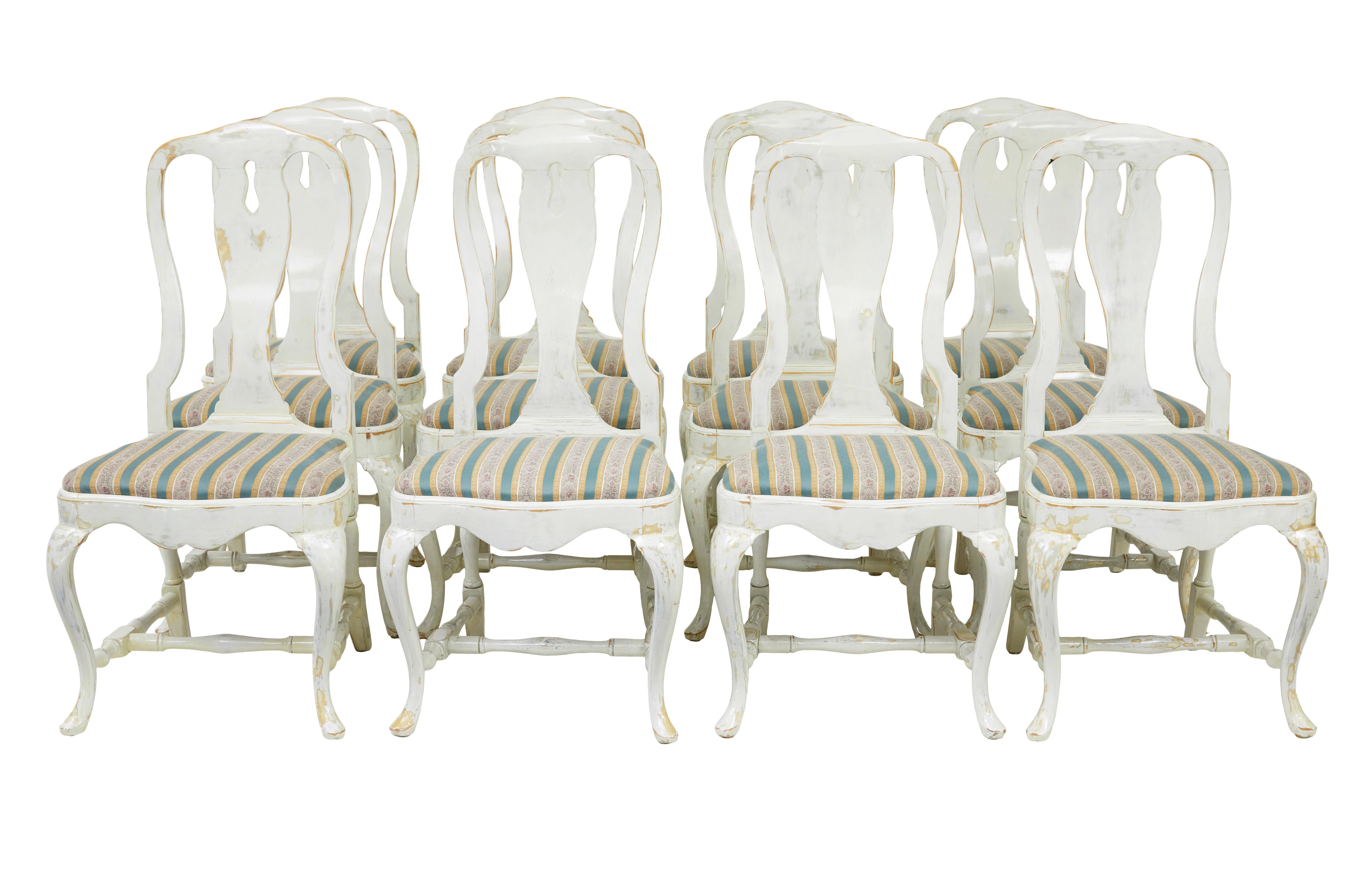 Set of 14 lacquered queen anne influenced dining chairs circa 1920.

Set comprises of 12 single chairs and 2 carver armchairs.  Made in beech and later painted white, this paint has been rubbed through in places to create a worn effect with a