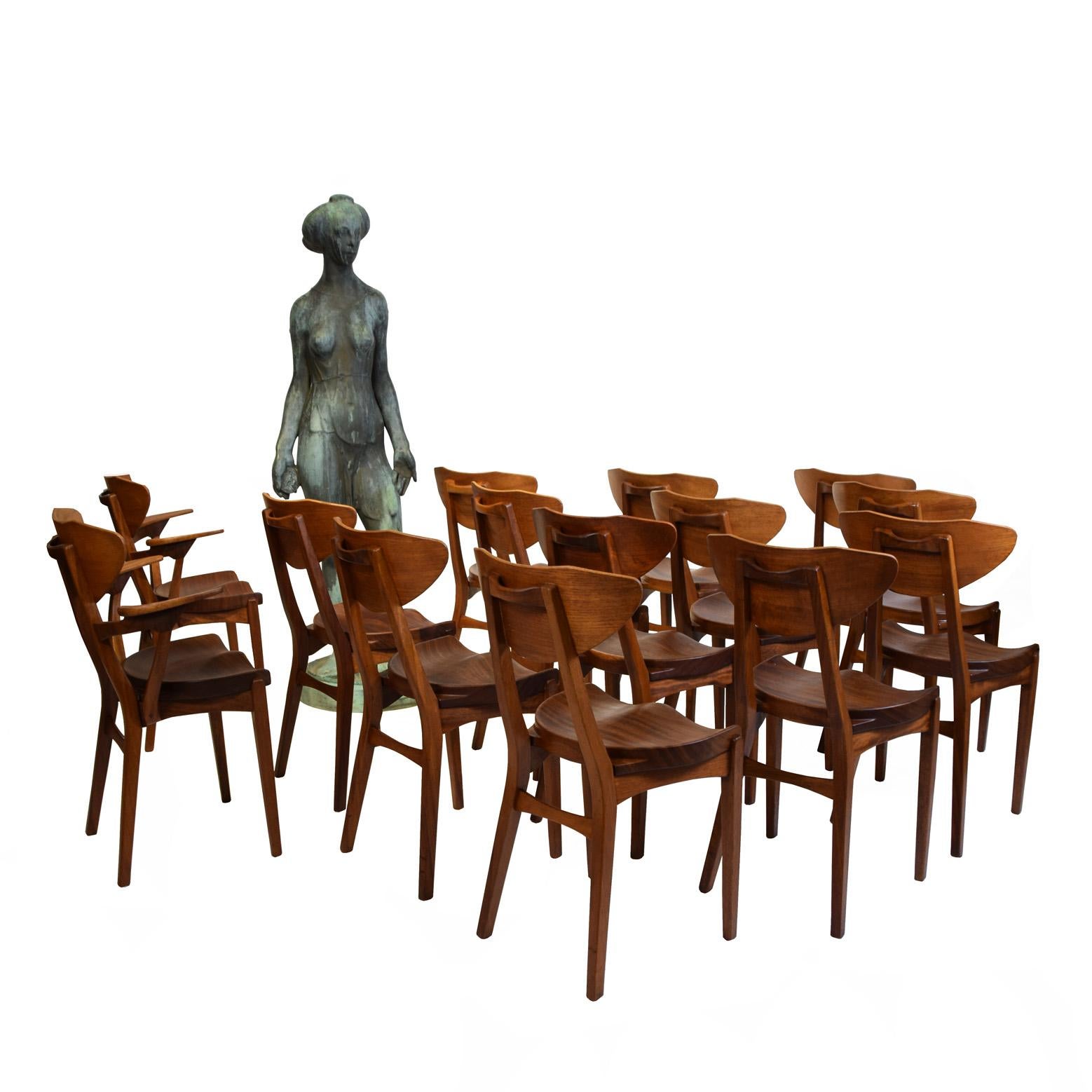 12 solid teak dining chairs and 2 armchairs. Saddle-shaped seat, back with handle. Produced by A. Hansen & Søn. Literature: Møbelfabrikanten, June 1951. Minor signs of wear.