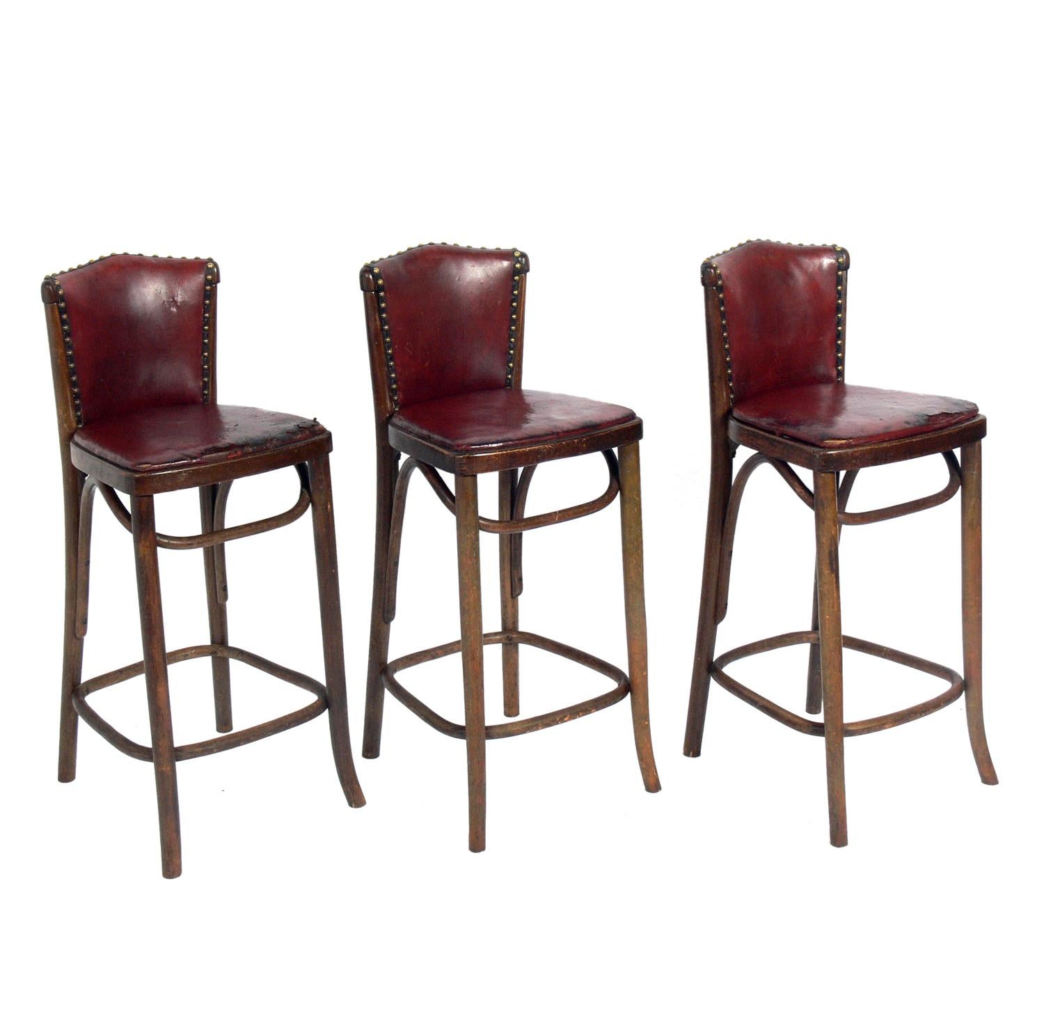 Set of Bentwood Bar Stools, circa 1930s. They retain their original cognac leather upholstery with brass nailhead trim. These stools show a lot of distressed patina and wear, especially at the front of the seats, where some of the leather is missing
