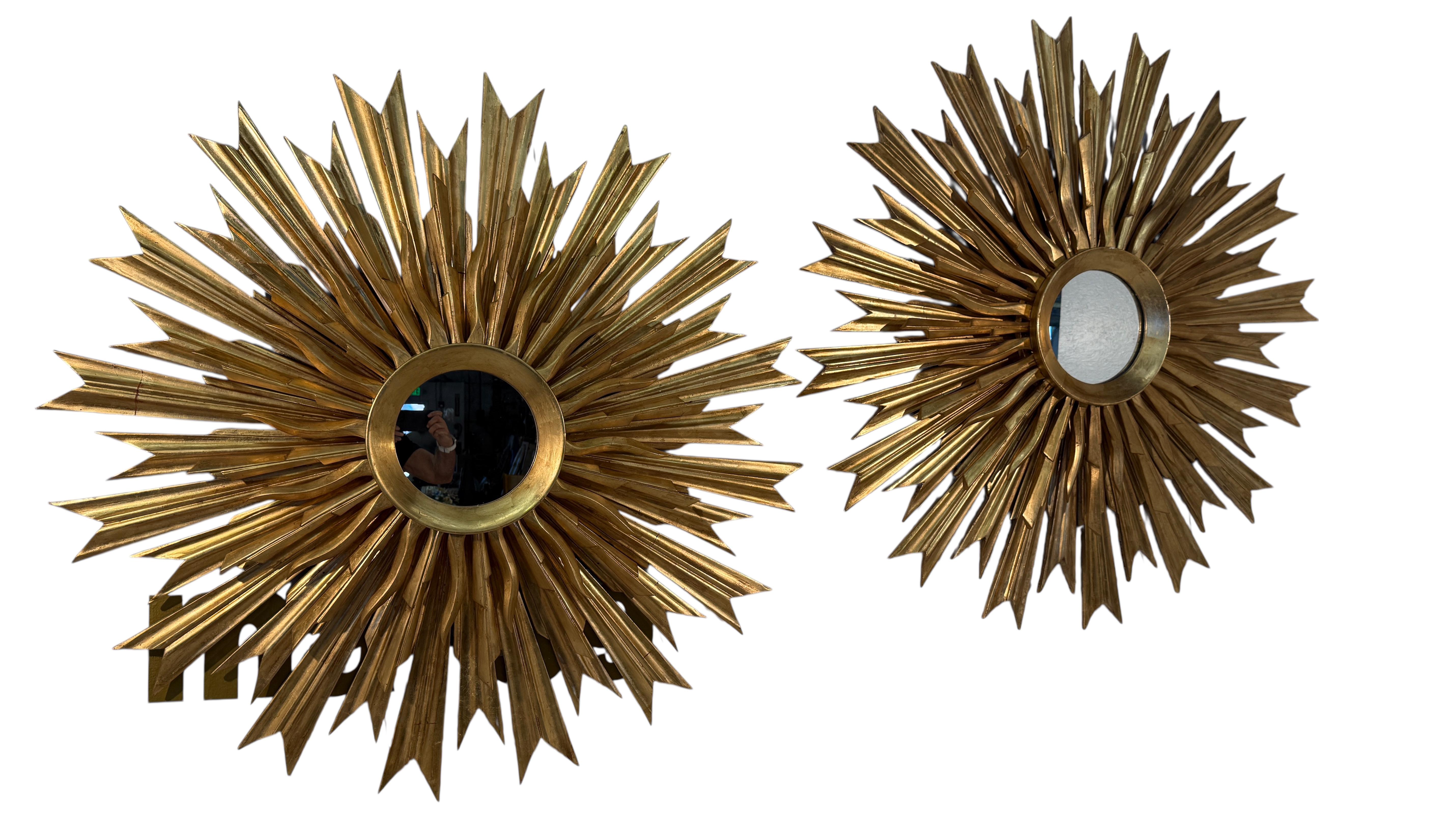 Il set di 2 suggestivi specchi da parete presenta un elaborato design a raggiera, con uno specchio centrale circolare circondato da una serie di raggi allungati e affusolati. Ogni raggio è scolpito meticolosamente con sfaccettature angolari, creando
