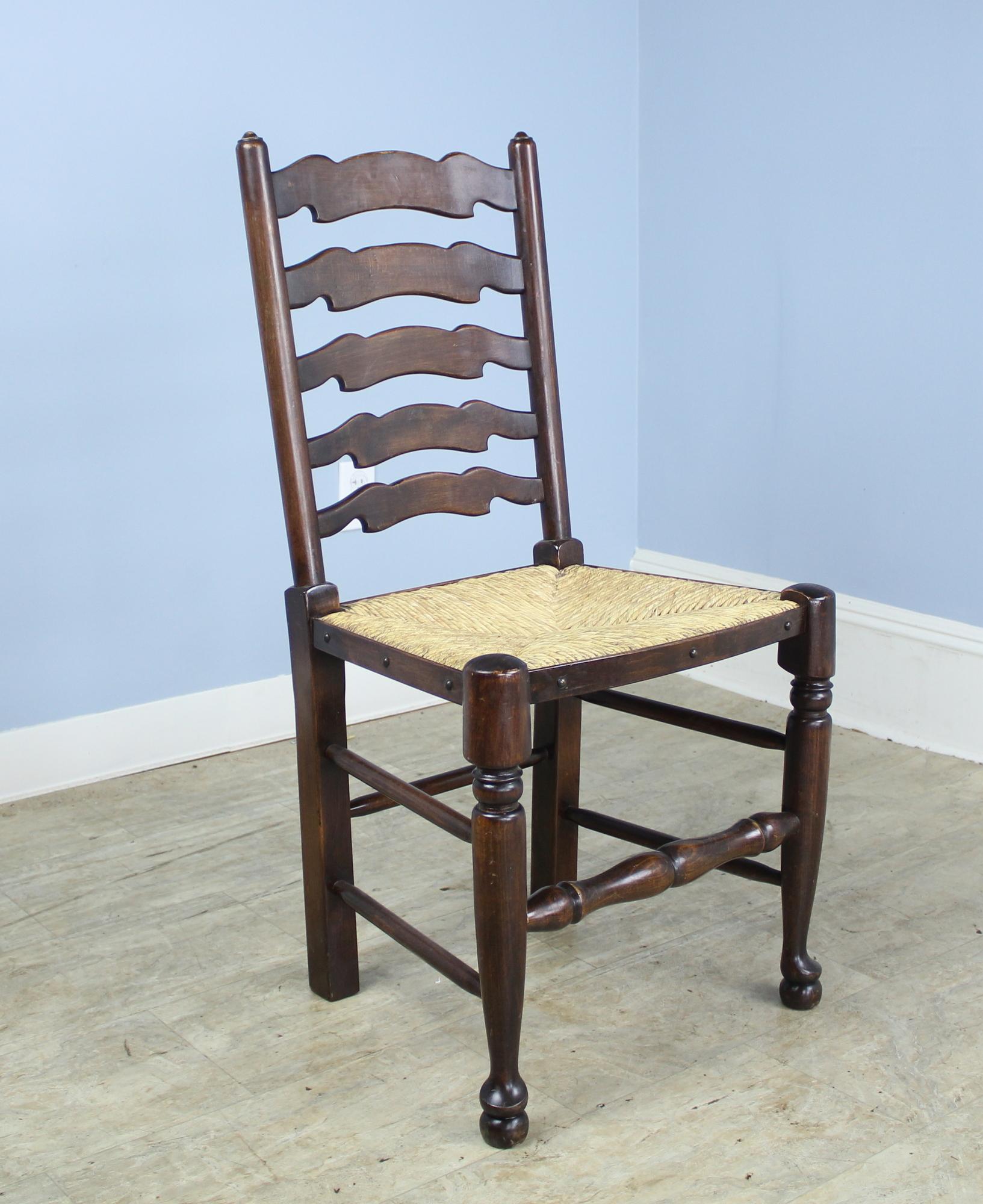An elegant country look. Set of two arm and six side English wavy back ladder chairs in dark oak. The rush is in good antique condition, and the chairs are quite comfortable as the backs have a slight recline. Interesting bullet motif around the