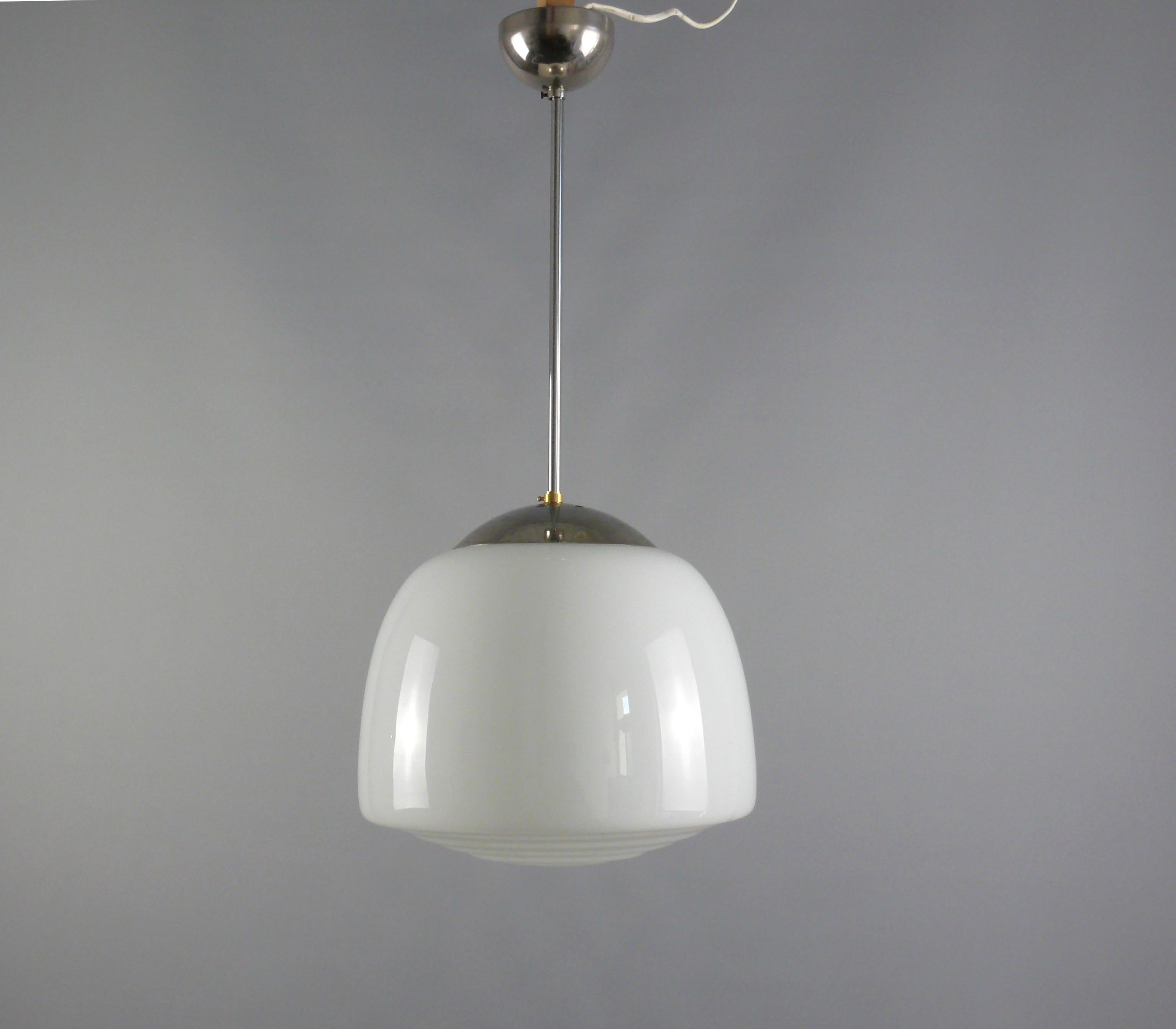 2 elegant Bauhaus pendant lights with chrome-plated/nickel-plated suspension and stepped, trapezoidal opal glass lampshade. The lamps date from the first half of the 20th century. The two identical opal glass shades are in good condition. The