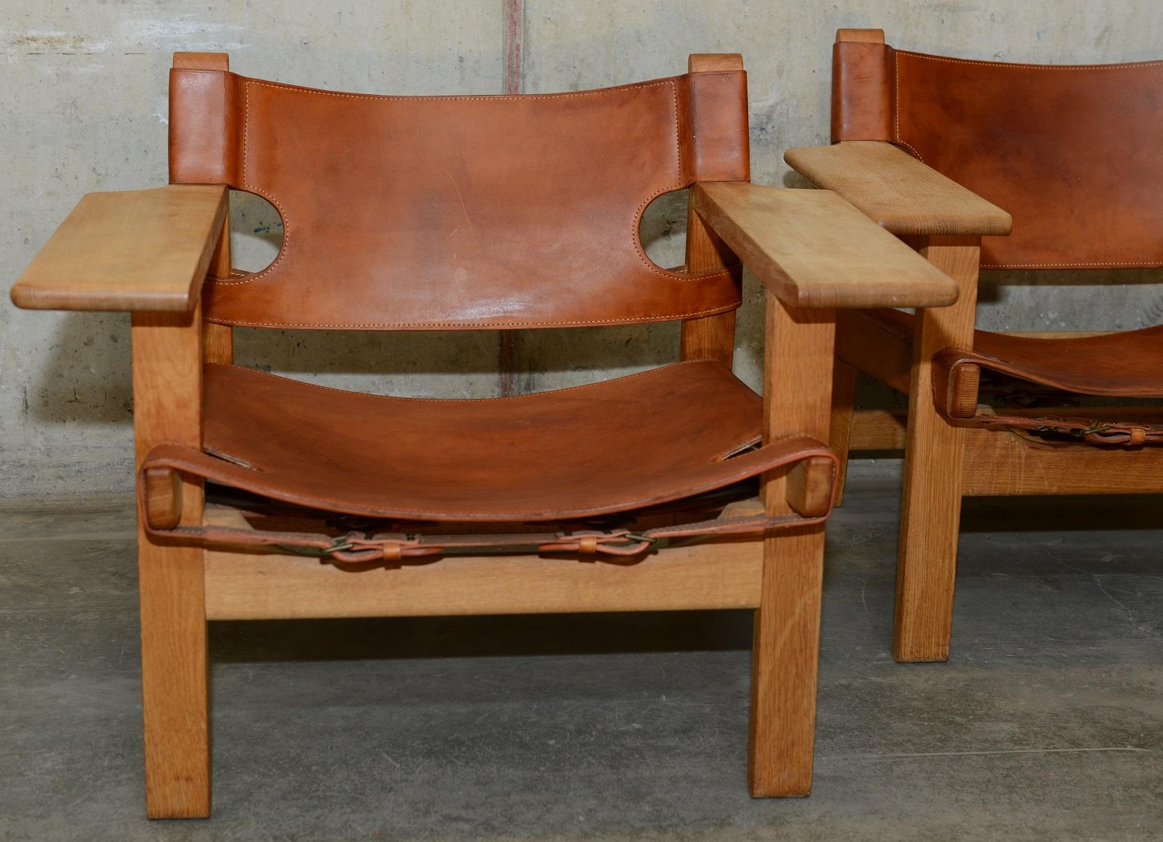 2 oak and cognac leather Spanish chairs designed by Danish Børge Mogensen. The chairs feature wide armrests and leather details. Robust but still elegant design. A true Scandinavian Modern / midcentury Classic. These 2 specific chairs were produced