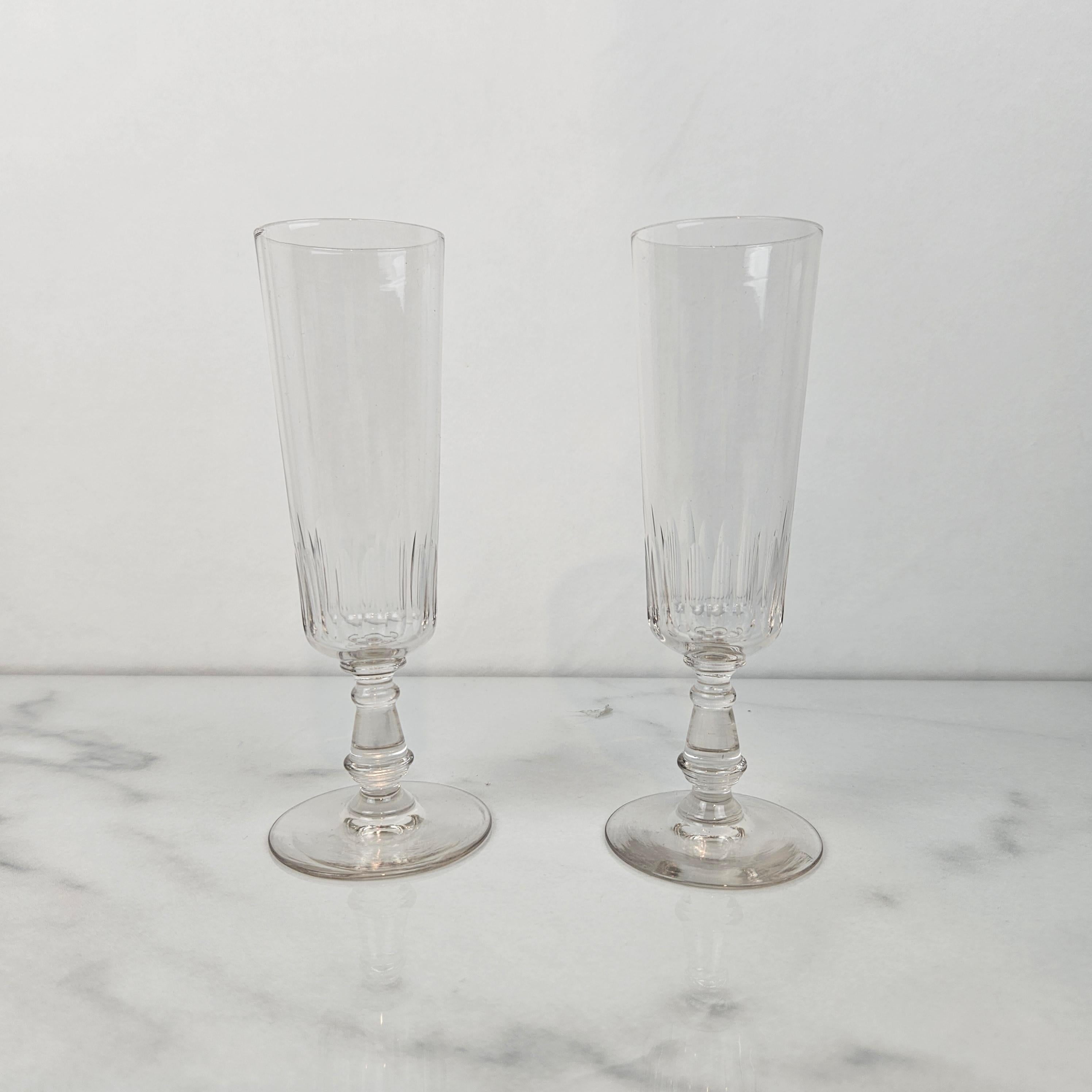 Un ensemble raffiné de coupes à champagne françaises anciennes, fabriquées en verre clair vers 1900. 
Les deux flûtes sont dotées d'une coupe inférieure magnifiquement taillée et d'une tige ornée de détails décoratifs, offrant à la fois un intérêt