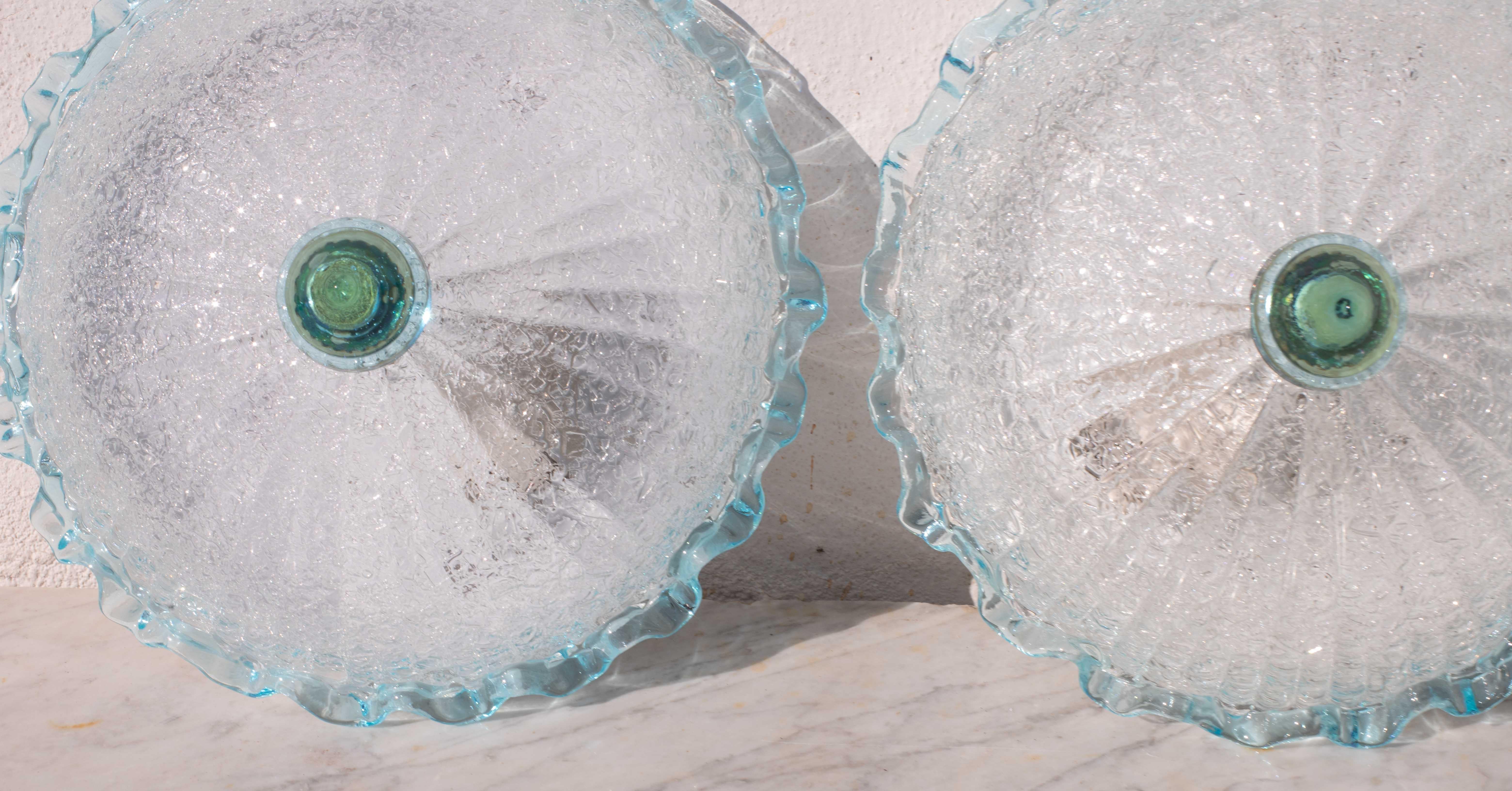 Lot de 2 superbes plafonniers Murano de couleur bleu et transparent/argent.
Le plafonnier se compose de deux éléments en verre, la plaque centrale et l'élément bas bleu.
La plaque centrale est entourée d'une bande bleue ondulée typique de la facture