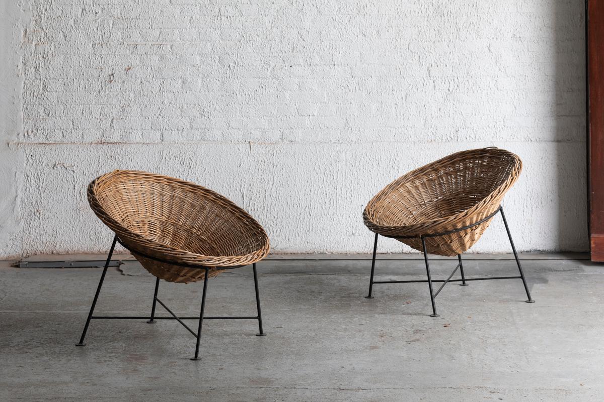 Set of 2 rattan lounge chairs, designed and produced in France around 1960. The design features a circular basket which rests upon a black lacquered, metal wire frame. A comfortable pair which could be potentially used as outdoor garden chairs. In