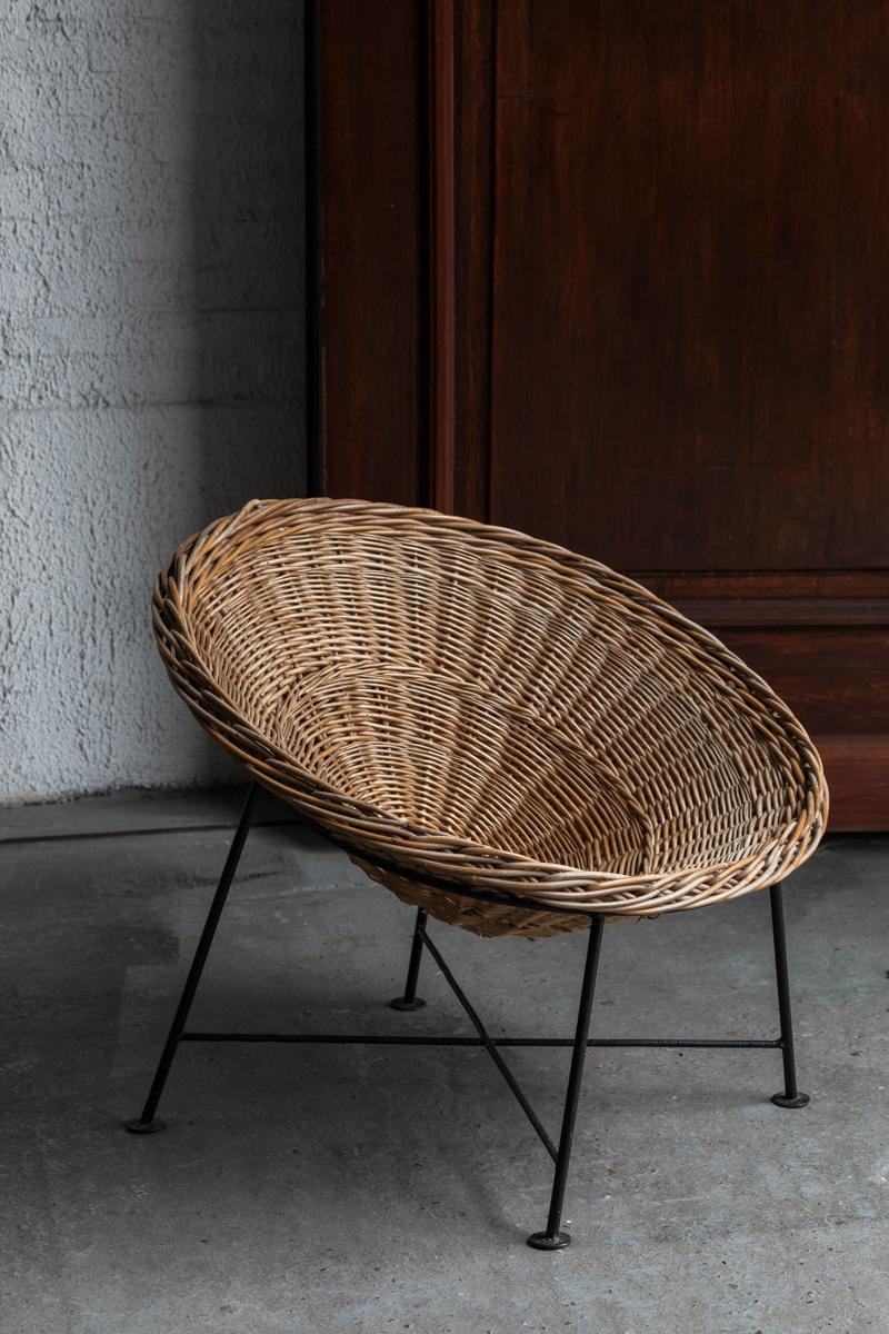 Set of 2 rattan lounge chairs, designed and produced in France around 1960. The design features a circular basket which rests upon a black lacquered, metal wire frame. A comfortable pair which could be potentially used as outdoor garden chairs. In