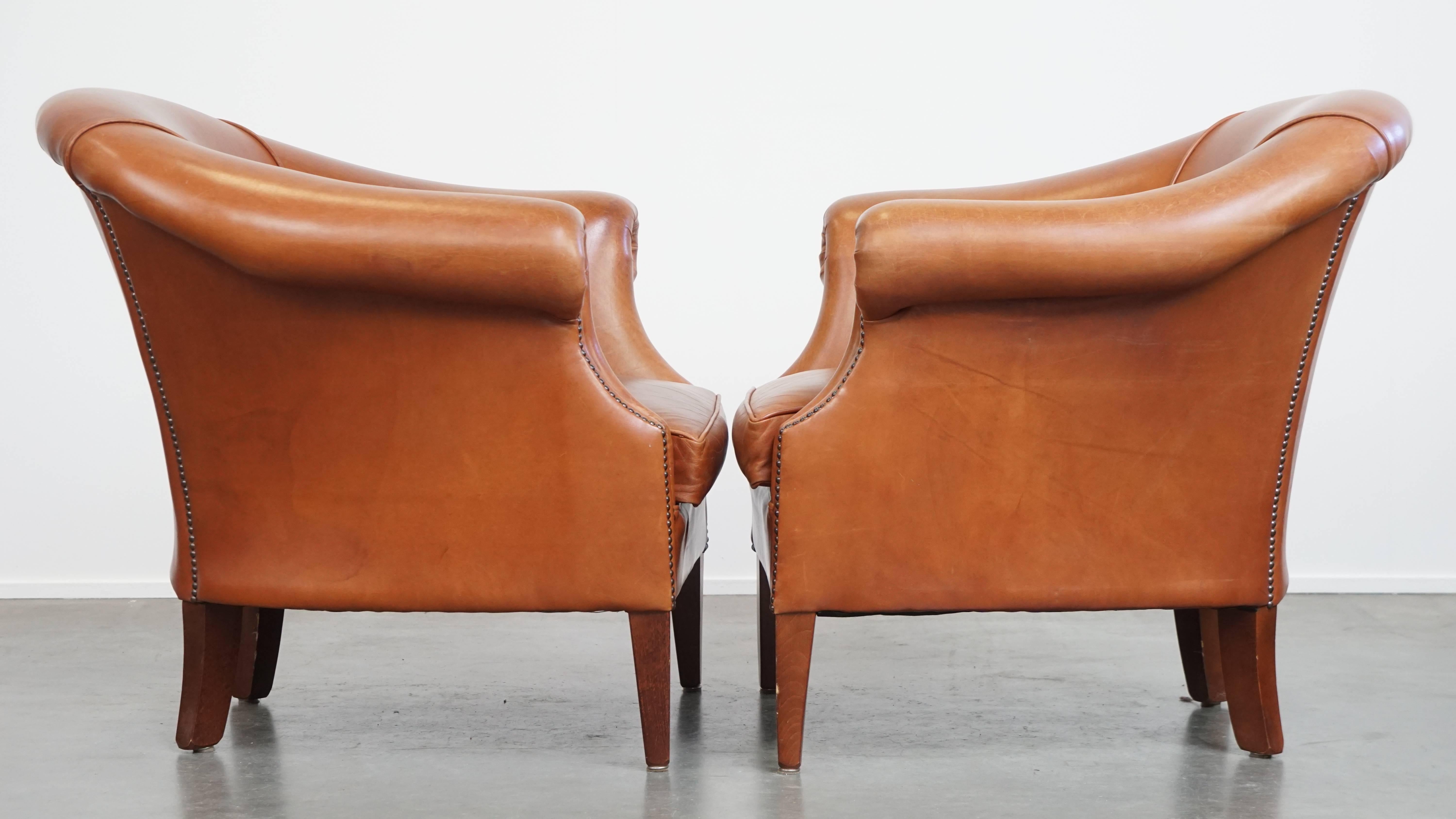 Offered here is this set of 2 cognac-colored cowhide leather club armchairs, in good condition, featuring a decorative stud finish. 

These comfortable English-style club chairs have a timeless and universally appealing look, making them an easy fit