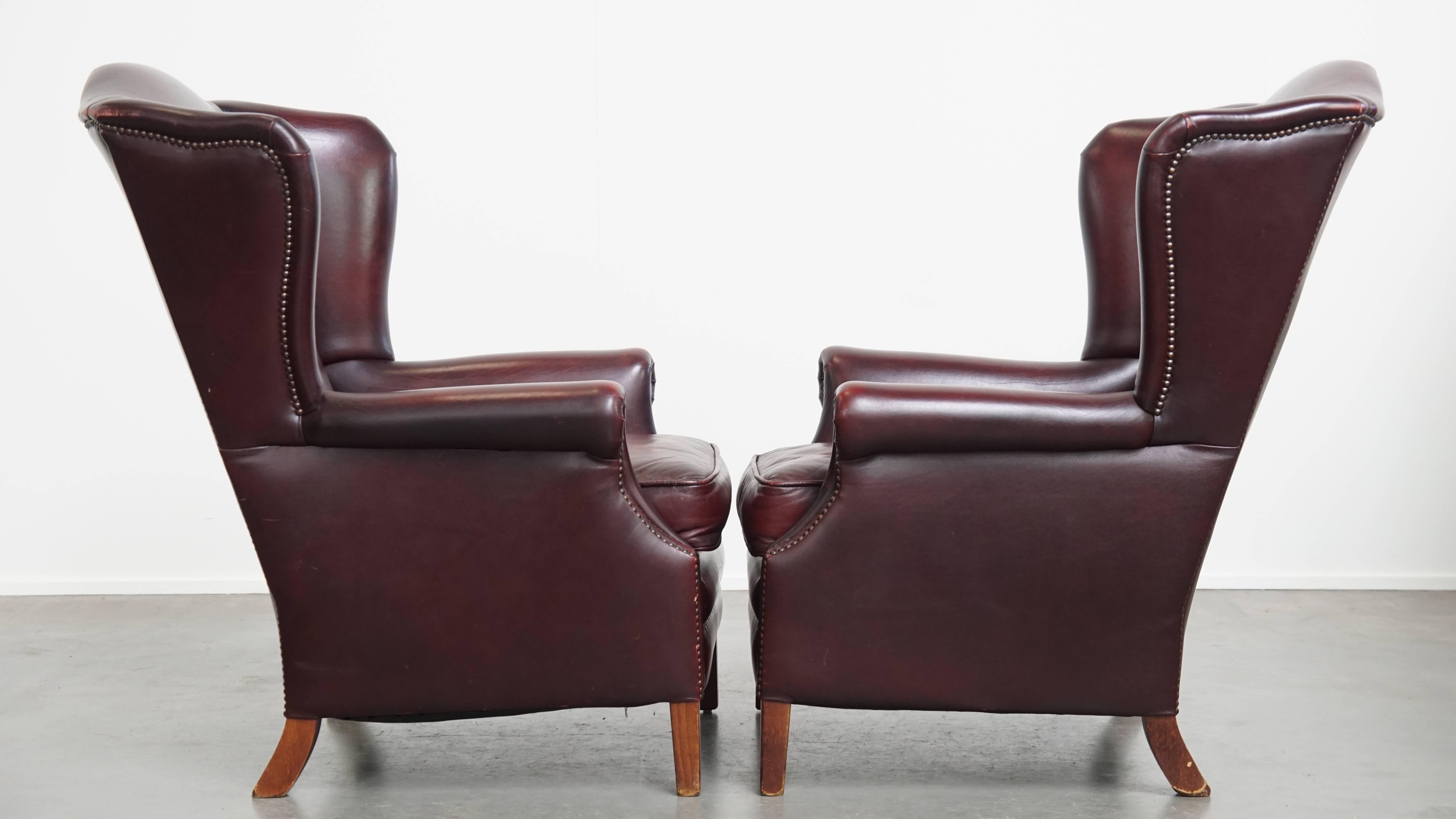 Offered: this luxurious set of two comfortable burgundy leather wingback armchairs in English style, featuring a stunning patina. Made from high-quality cowhide leather and finished with decorative studs, these chairs exude classic elegance.

Each