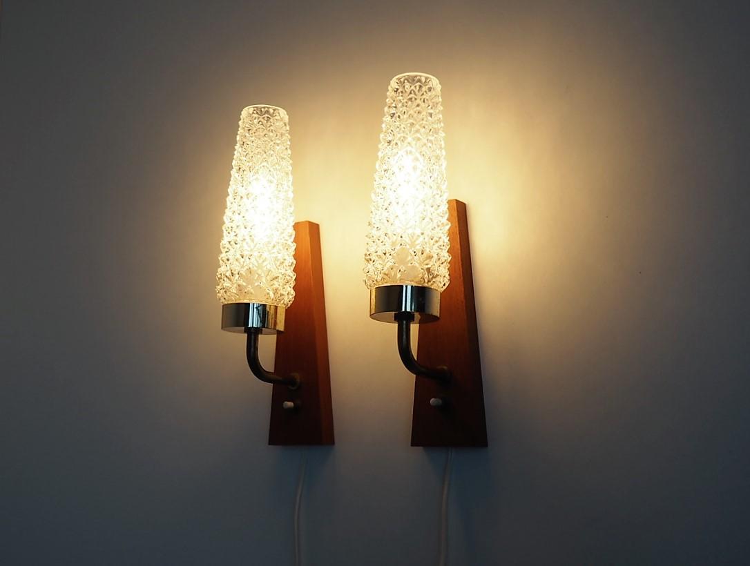 Set of 2 wall sconces with wall base made in teak and a glass tube with beautiful molded pattern that covers for the bulb. The light is being beautifully reflected from the glass shades.

The sconces are made by a Danish manufacturer called Stil