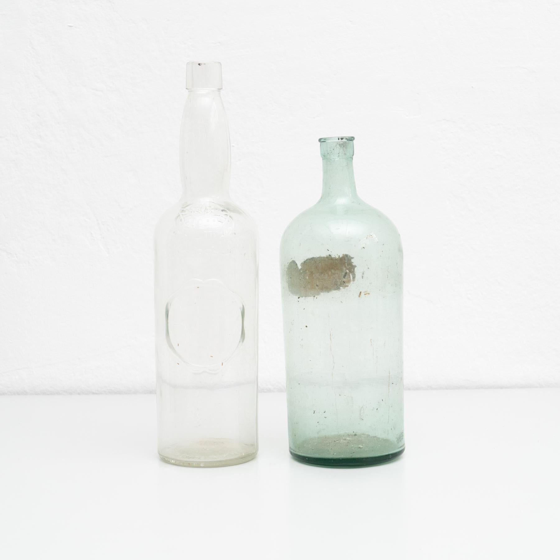 Conjunto de 2 botellas de cristal de principios del siglo XX.    Fabricante desconocido, España.    En su estado original, con pequeños desgastes propios de la edad y el uso, conserva una hermosa pátina.    Materiales:  Vidrio.   