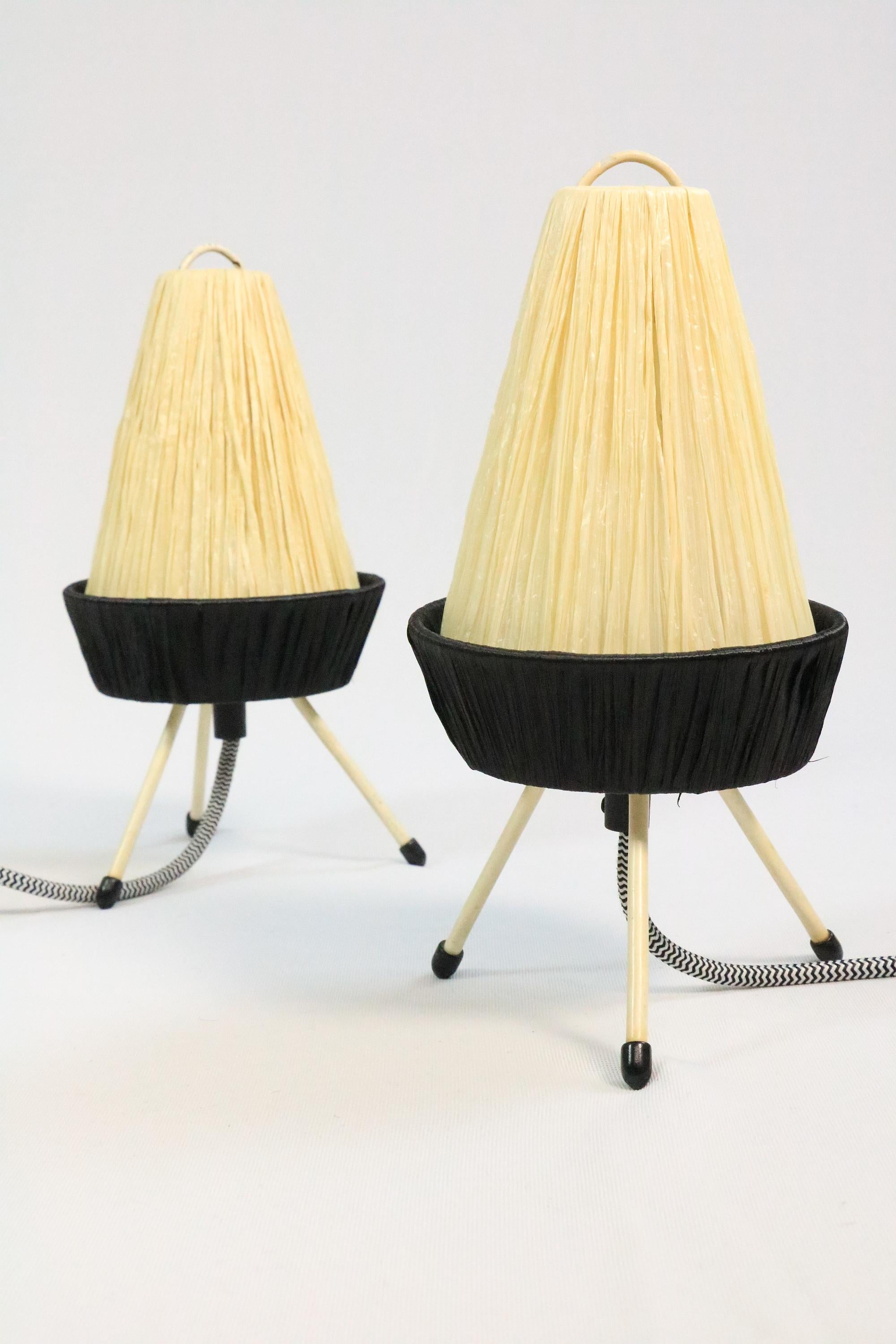 Two enchanting little table lamps made from raffia. Each stands on three filigree legs. 
A really typical 50s Design.
 
Create a charming light.
New wiring with black and white textile cable.
 
In very good condition, with slight chips in the paint