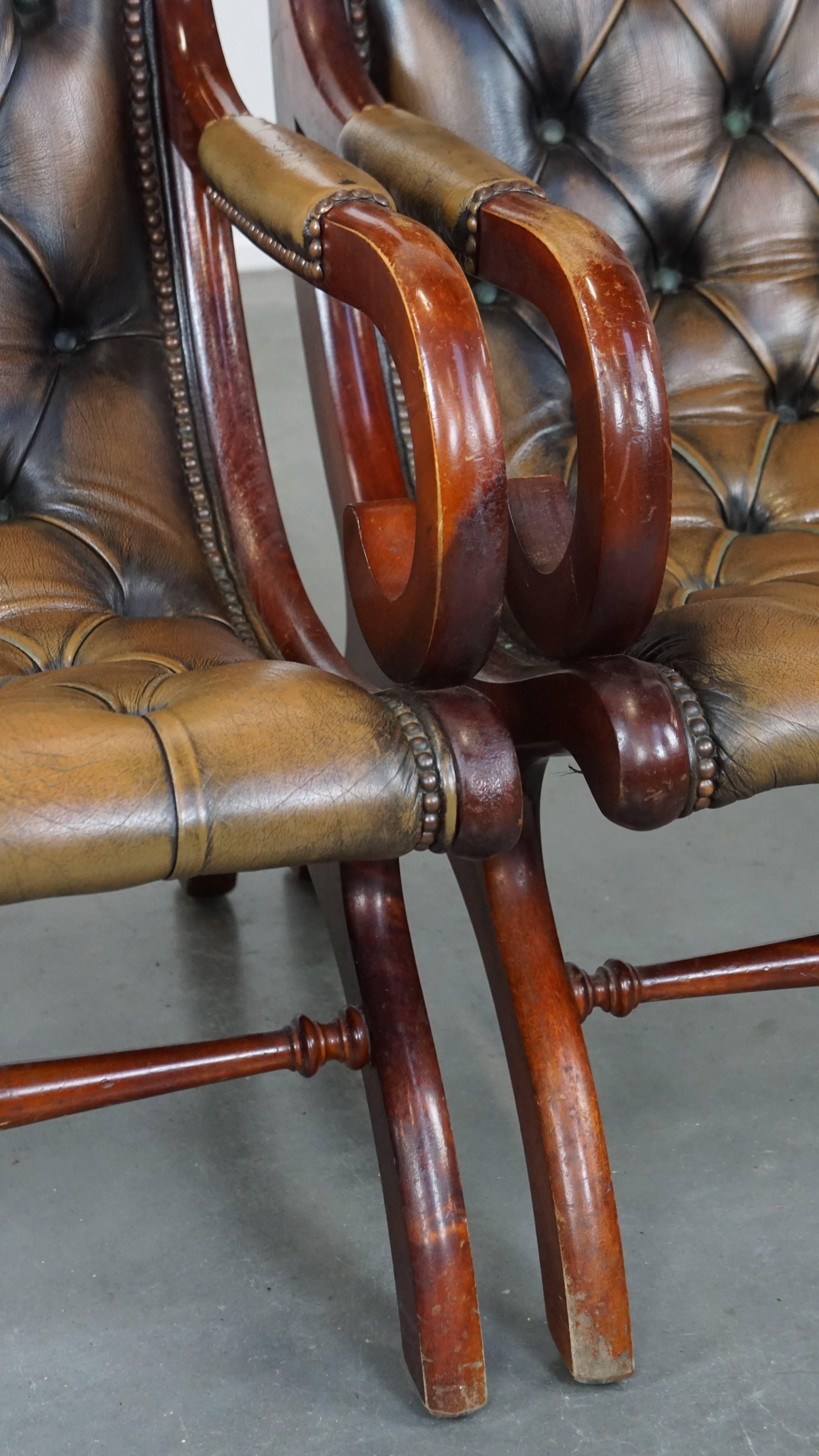 This set of two vintage cowhide leather Chesterfield armchairs exudes the beloved timeless English class and style. They feature a graceful design, a bold green color, and are beautifully finished with decorative nails. These armchairs are combined