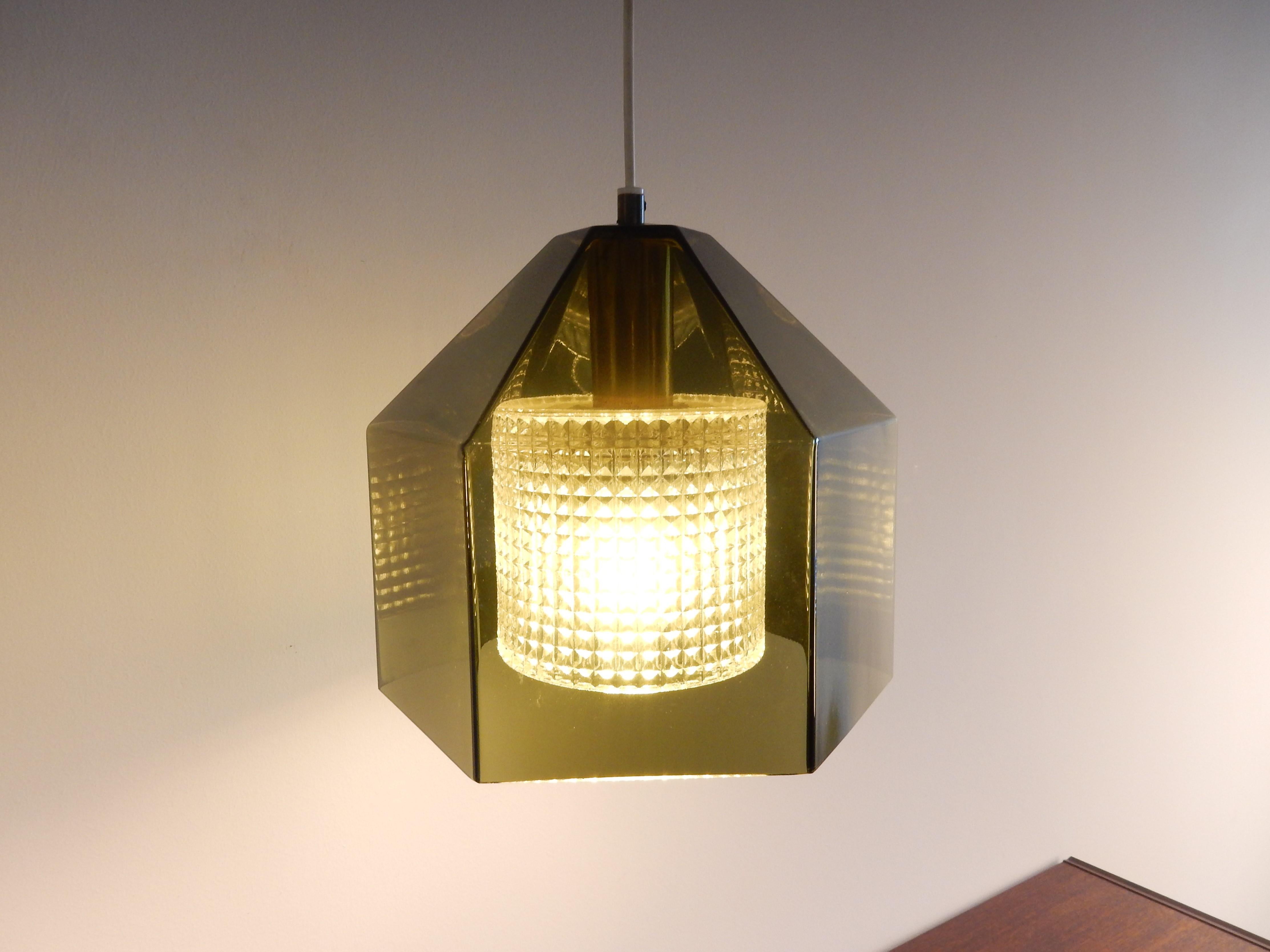 This beautiful and elegant pendant lamp was designed by Carl Fagerlund for Orrefors in Sweden in the 1960s. It has a hexagonal green-grey glass exterior shade and a smaller patterned clear glass interior shade. The lamp gives a good and clear