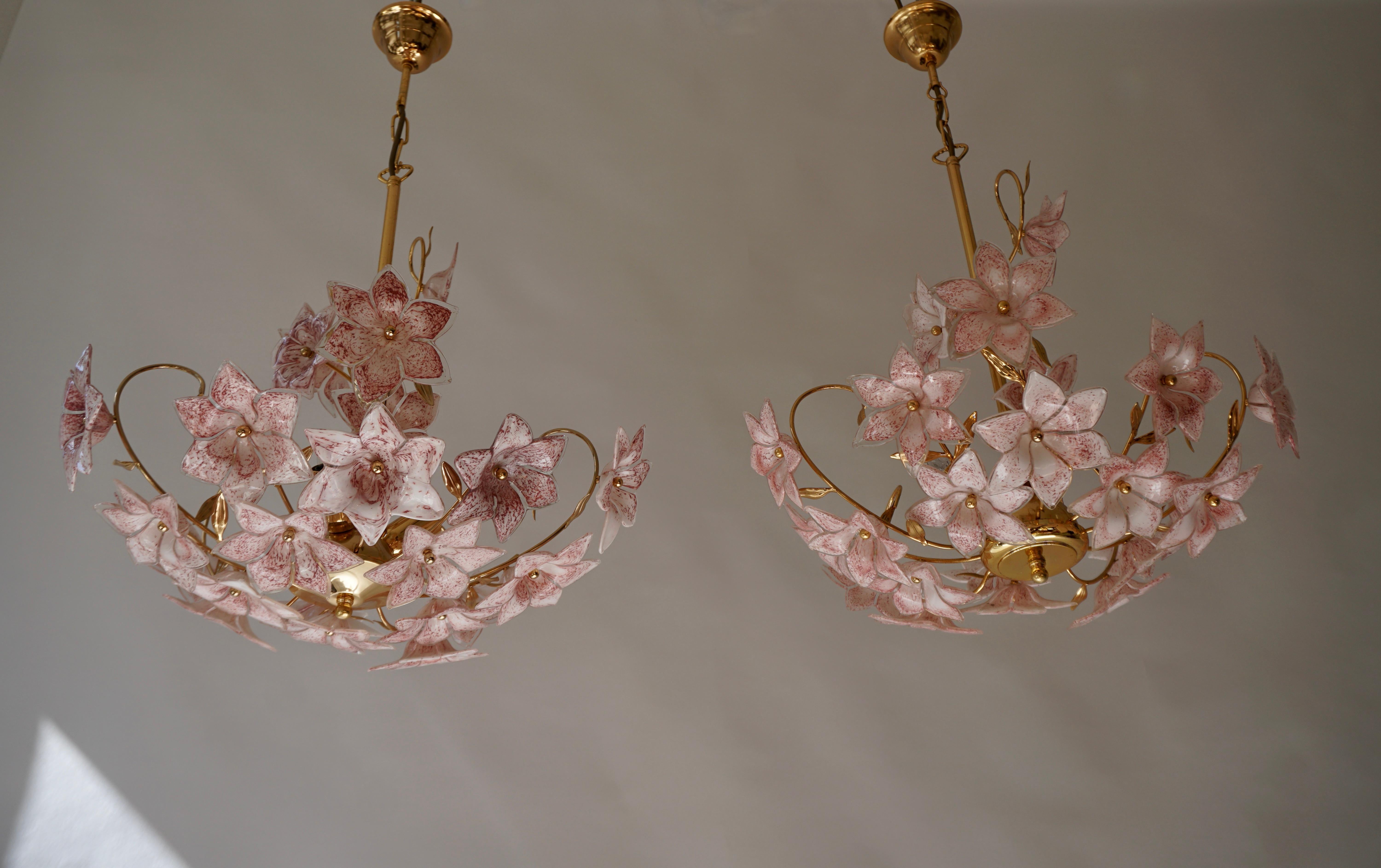 Set of 2 Italian brass chandeliers whit white pink Murano colored glass flowers.

The chandeliers are almost exactly the same, only the round brass plate at the bottom has a slightly different shape.
And the glass Murano flowers also have a slightly