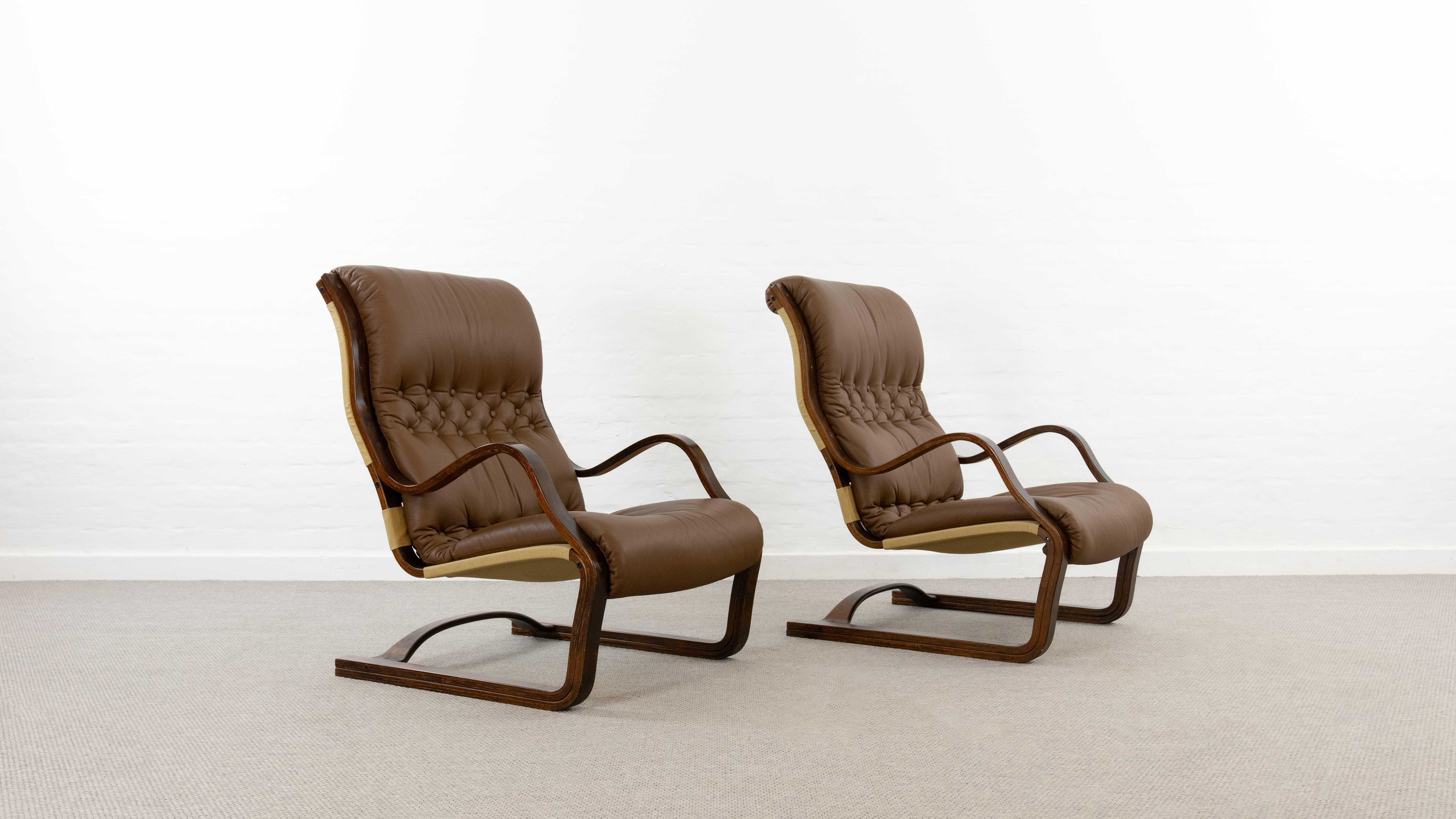Ensemble de 2 fauteuils Koivutaru à suspension libre. Conçu en 1977 par Esko Pajamies pour Asko, Finlande. Rembourré dans son cuir boutonné marron d'origine. La chaise de cheminée idéale. Très belle formation en bois courbé des accoudoirs et du
