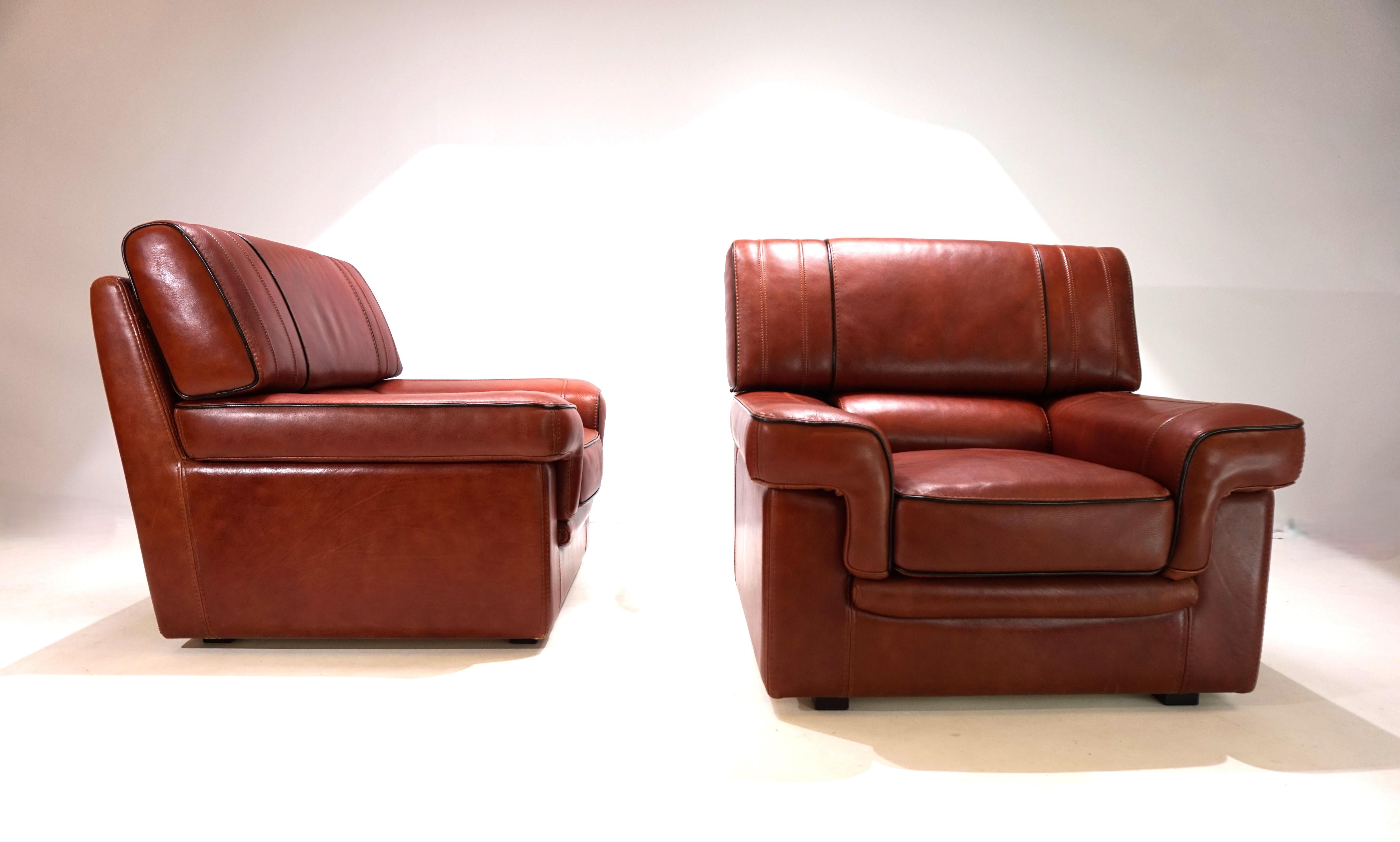 The two leather armchairs have a beautiful, warm cognac-colored leather tone and are in first-class condition. The armchairs are made of the highest quality from 4-6 mm thick neck leather and are elaborately finished with black piping on the corners