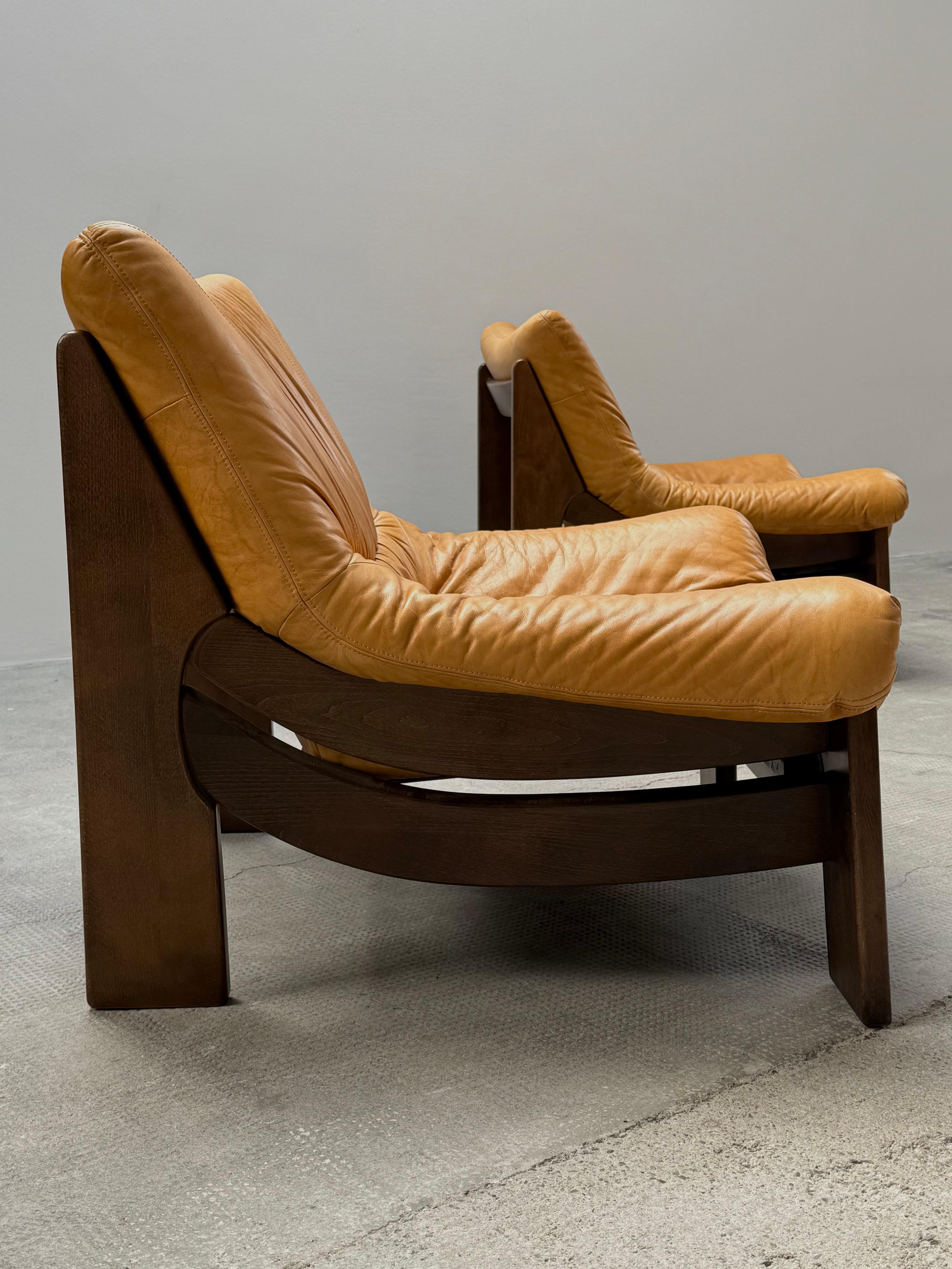 Fantastic set of two brutalist armchairs in leather and solid oak wood frame in a attributed to Maison Regain, France, 1970s.

In excellent original condition. Very expansive, solid, heavy, and very comfortable to sit in.

The 3-seater sofa is