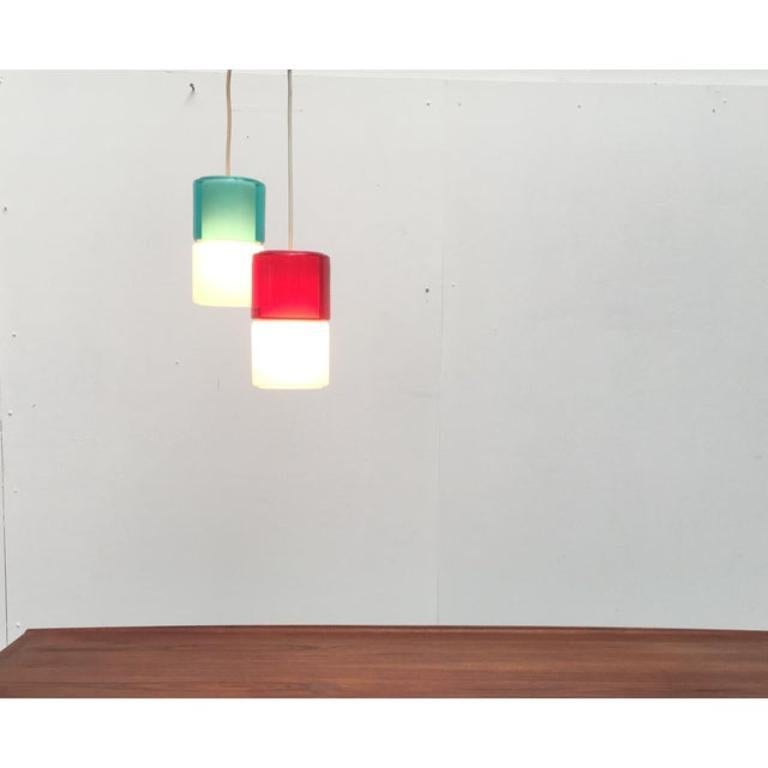 Coloured glass pendulum from the renowned manufacturer Putzler.

The whole design language seems rather Scandinavian. The simple form of the lamps is broken up by a play with colour and transparency. The cylinder made of coloured transparent glass,