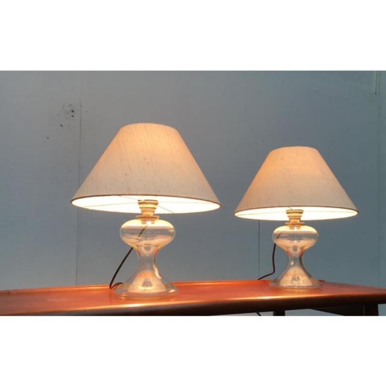 Uno de los primeros diseños del famoso diseñador de luminarias Ingo Maurer, de finales de los años 60.

Un diseño elegante y clásico. La base es de cristal transparente. La pantalla tiene una forma sencilla y clásica. Está recubierta por fuera con