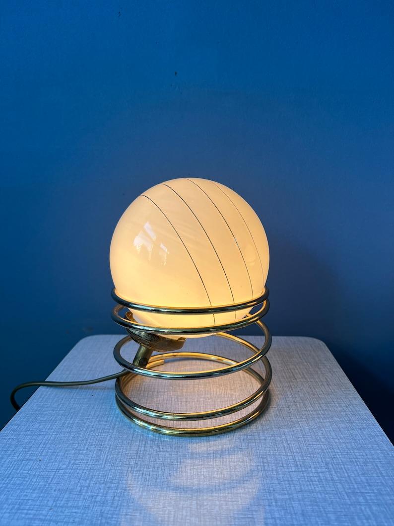 Set of 2 mid century hollywood regency eyeball table lamps with golden spiral base and opaline glass shade. The shades can be placed in the metal rings in any way desirable. The lamps require E14 lightbulbs and currently have EU-plugs.

Additional