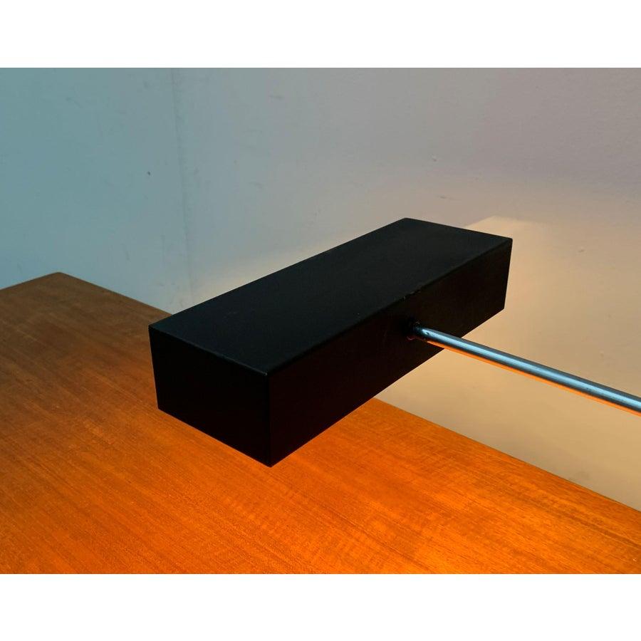 Minimalist mid century table lamps.

Cubic shapes permeate this design. The shades show the shape of a long black cuboid, open on the bottom. Color and shape is echoed in the heavy base plate. The vertical stem is mounted asymmetrically on the back