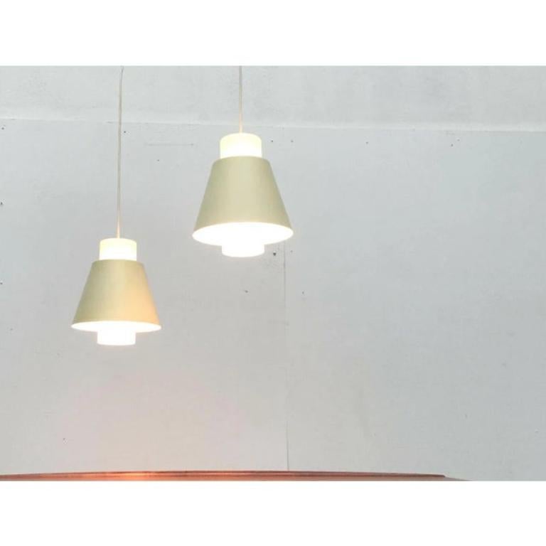 2 rare lampade a sospensione della metà del secolo scorso in vetro e metallo.

Il corpo della lampada è costituito principalmente da un cilindro di vetro smerigliato che funge da diffusore. Le cappe metalliche coniche, che fungono da anelli ciechi,