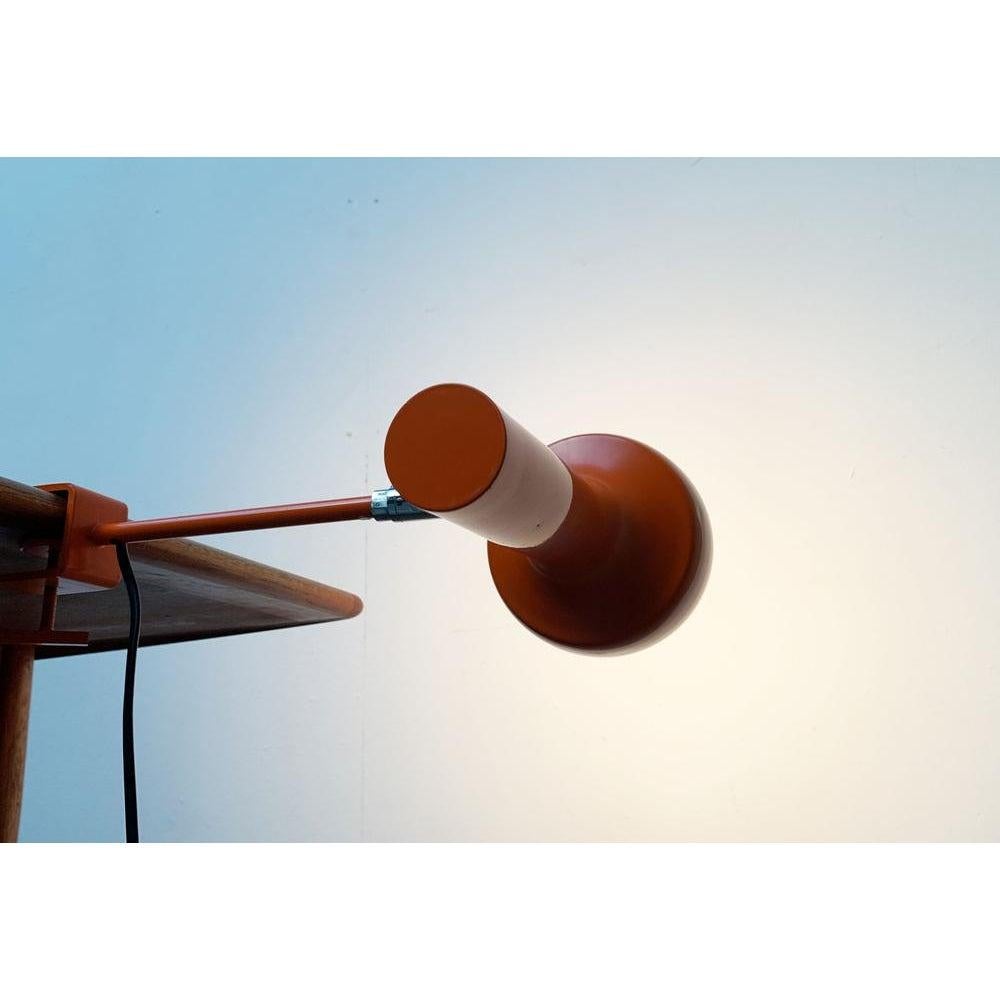 Luces de sujeción minimalistas de Swisslamps en un color especial. Aquí en una versión temprana con un diseño excepcional de la pinza de mesa. Un diseño sencillo y sobrio. La cabeza de la luminaria tiene forma de radiador con una llamativa pantalla.