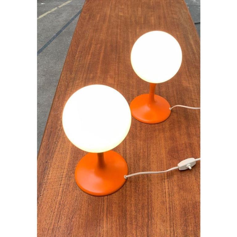 Tischleuchten des Schweizer Herstellers Temde nach einem Entwurf von Renee Nele.

Schlichte Tischlampen in einer auffälligen Farbe. Ein Opalglas-Globus auf einem elegant geschwungenen, trompetenförmigen Fuß. Der Fuß ist in Orange ausgeführt und geht