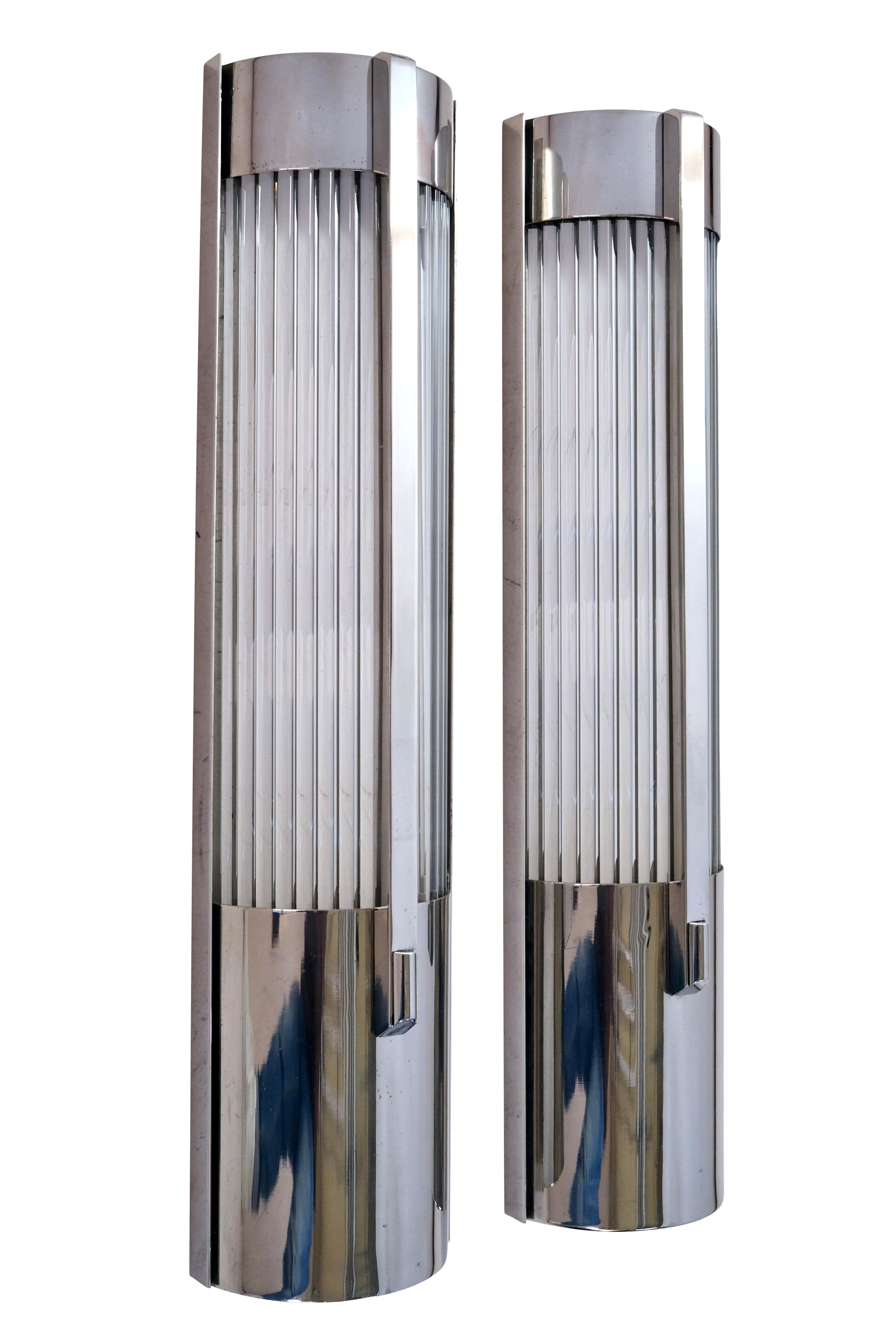 This striking pair of mid-century wall sconces, crafted in the 1960s, embodies the timeless elegance of Art Deco design, reimagined for the modern era. The sconces feature sleek, elongated glass rods encased in a frame with the original chrome