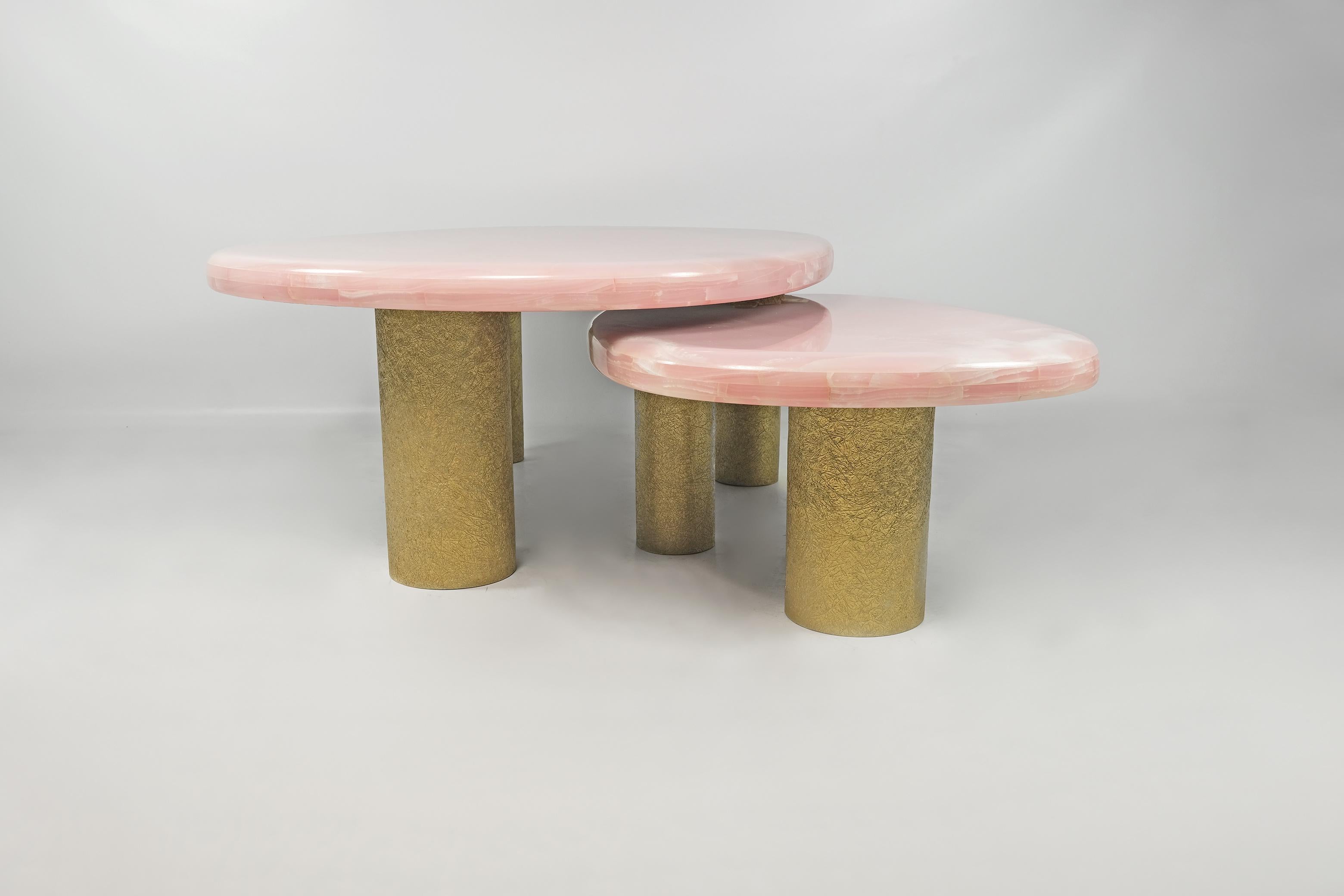 Cet ensemble de 2 tables basses est composé d'un plateau en onyx rose.

Chaque table a trois pieds cylindriques en bois avec une finition en fibre de verre brut doré.

Le dessus des tables est arrondi sur les bords, ce qui donne un style organique