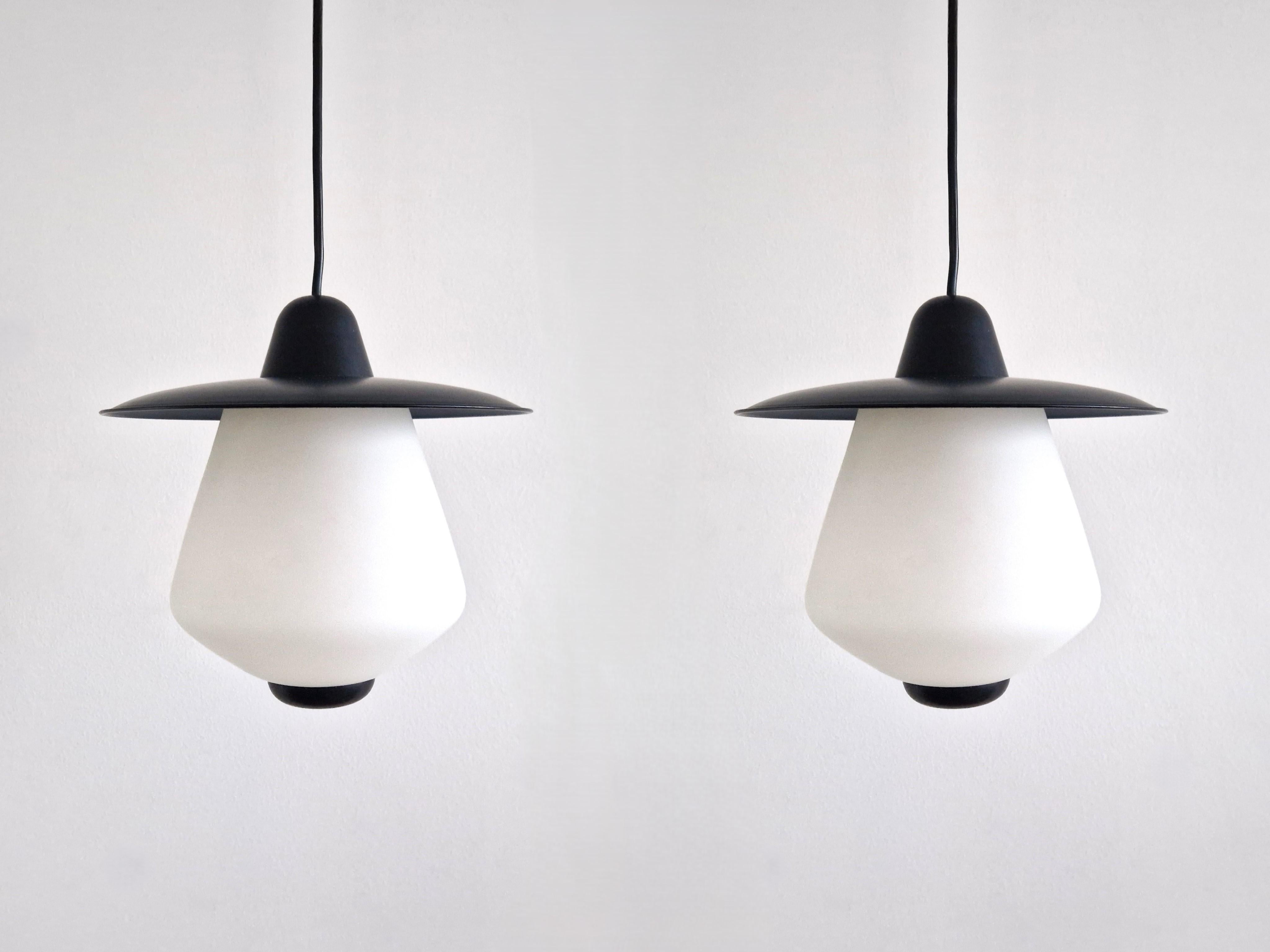 Questo modello di lampada a sospensione è spesso attribuito a Philips. Il paralume è in vetro opalino, la parte superiore in metallo laccato nero e la parte superiore e inferiore in plastica. Vendiamo questo set di 2 pezzi, tutti in ottime
