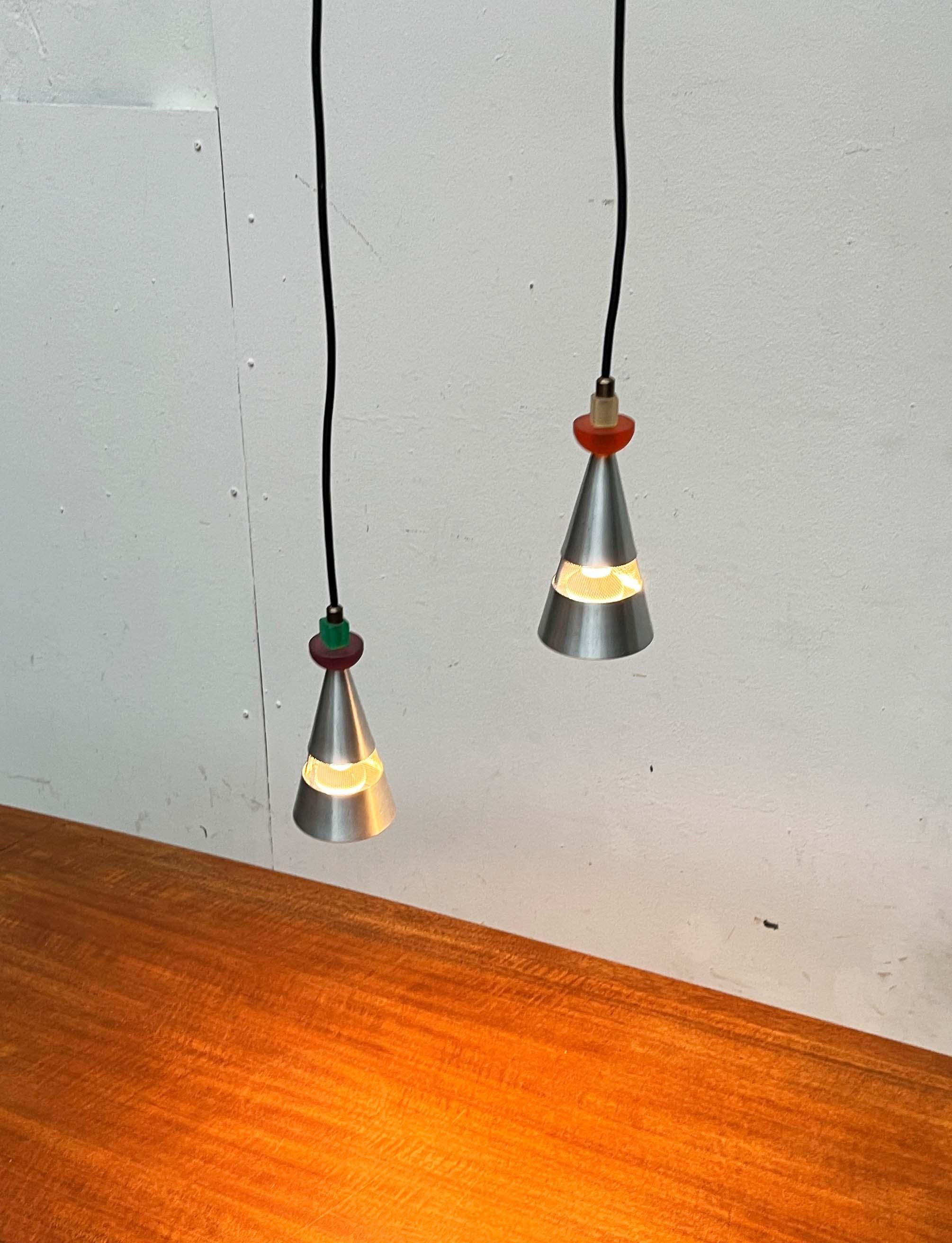Postmoderne Pendelleuchten des niederländischen Herstellers Studio Brandend Zand. 

Die Leuchtenkörper haben eine schlichte Kegelform. Die Schirme sind aus Aluminium gefertigt und im unteren Drittel durch ein eingesetztes Mesh aufgelöst. Besonders
