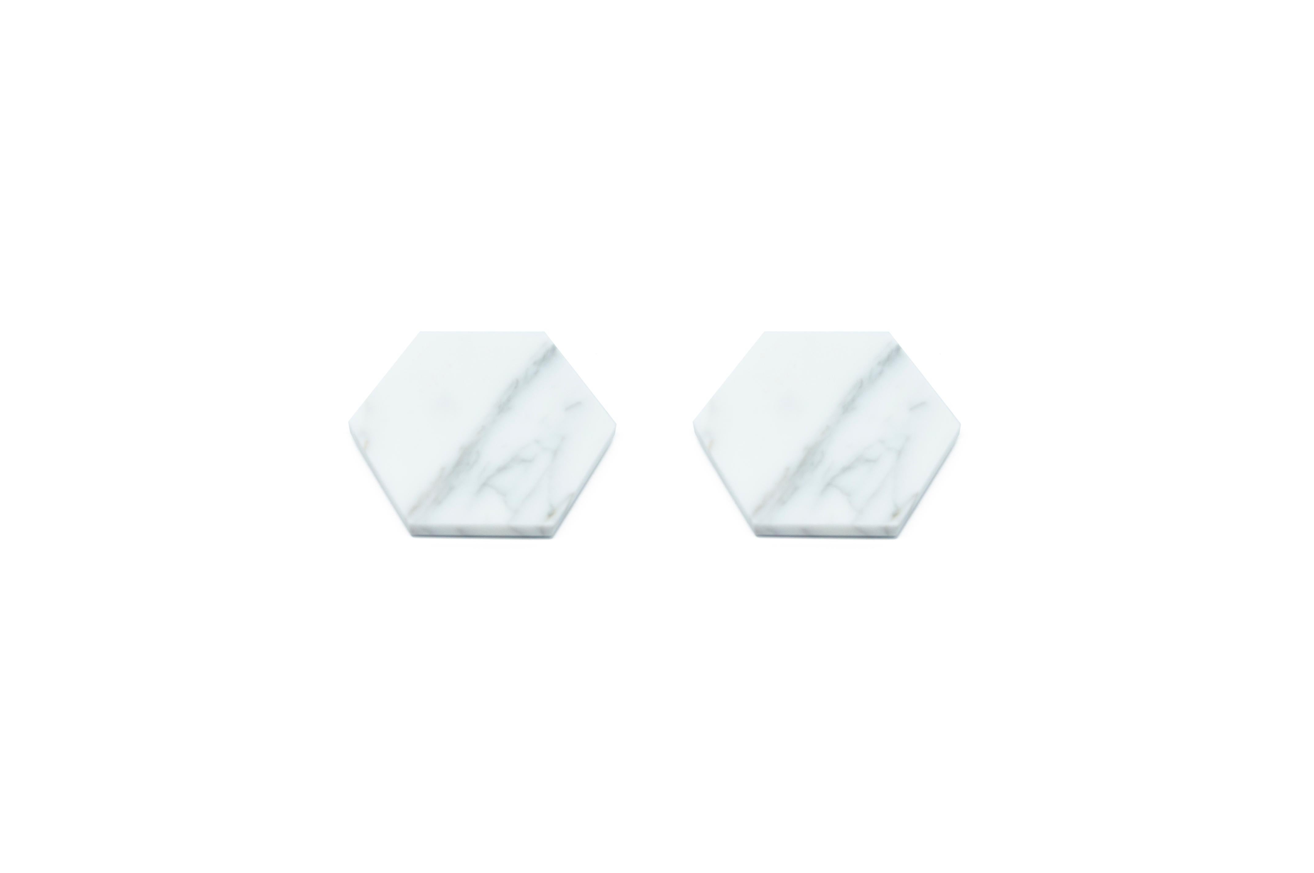 Set of 2 hexagonal white Carrara marble coasters with cork underneath. Each piece is in a way unique (every marble block is different in veins and shades) and handmade by Italian artisans specialized over generations in processing marble. Slight