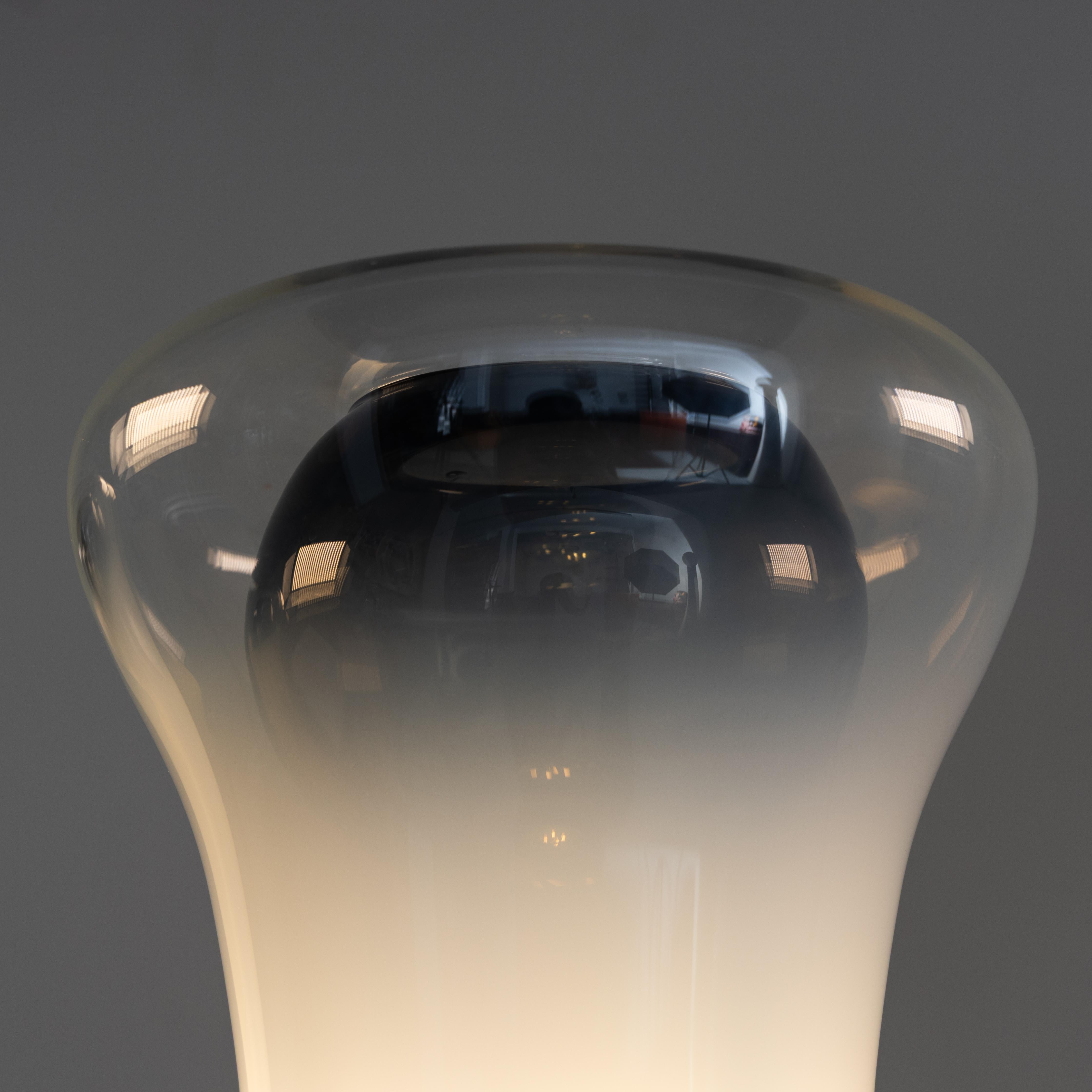 Disegnata da Angelo Mangiarotti e prodotta da Artemide nel 1967, la lampada è composta da un anello di metallo che sostiene un diffusore in vetro soffiato. Grazie alla sua superficie ombreggiata può attenuare la luce della sorgente luminosa. La