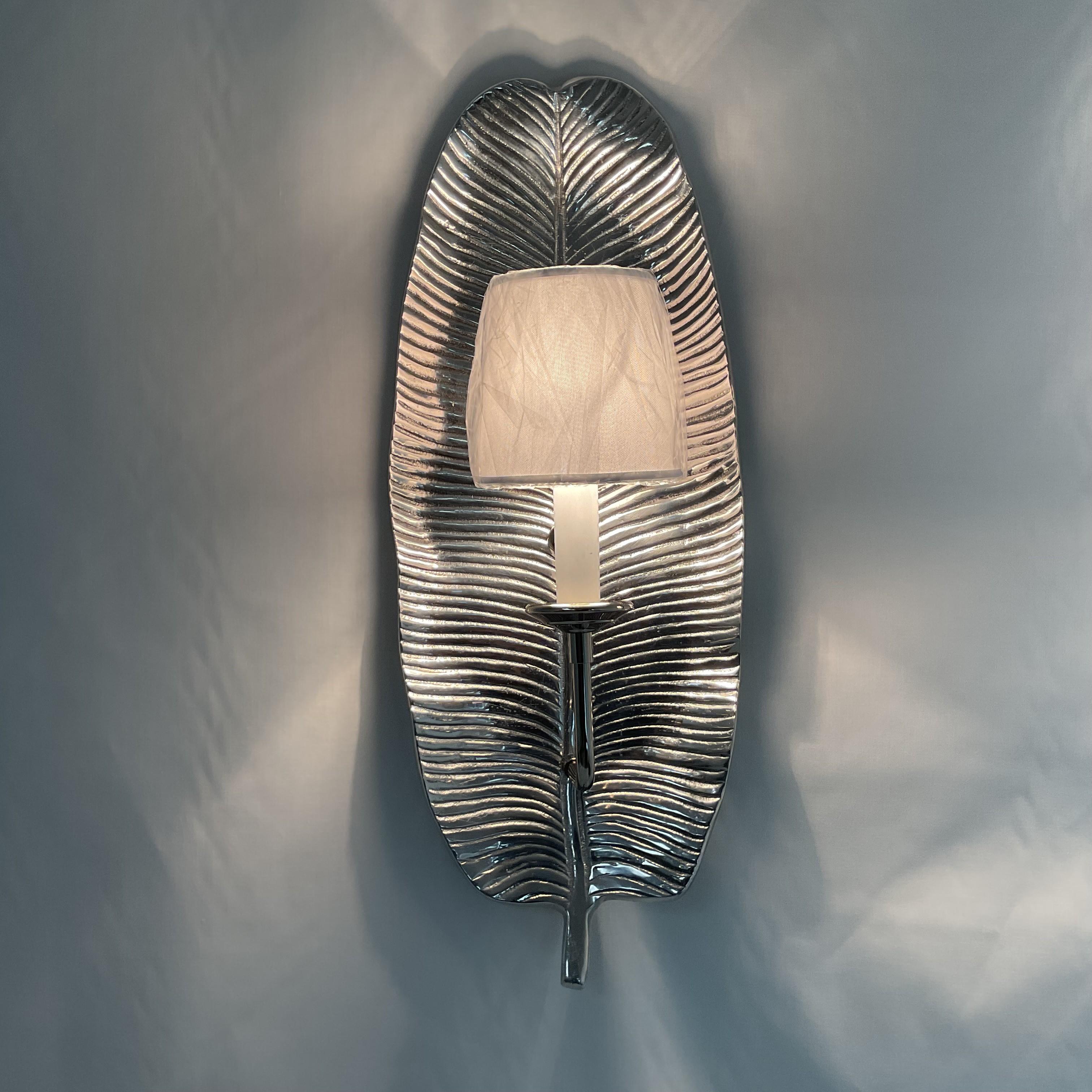 Elevate your interior decor with this stunning set of two silver wall sconces, each crafted with a sleek, leaf-inspired backplate. The sculpted metallic finish adds a contemporary touch, while the elegant white shades (still wrapped for protection)