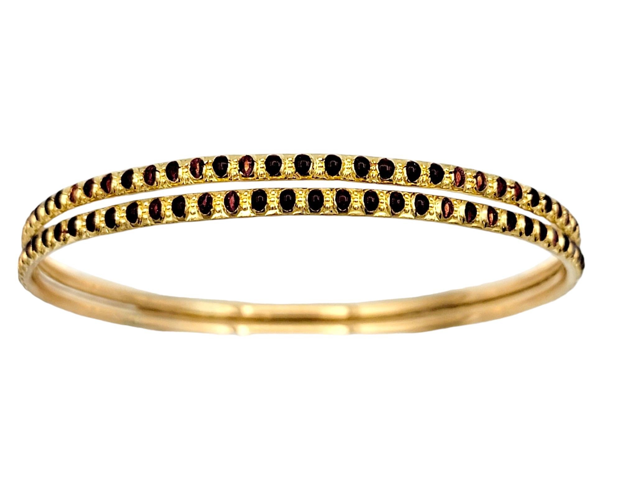 Introducing a stunning set of two narrow stacking bangle bracelets crafted in luxurious 22 karat yellow gold. These identical pieces are adorned with a mesmerizing dark red enamel dotted design that spans the entire length of the bracelets, adding a
