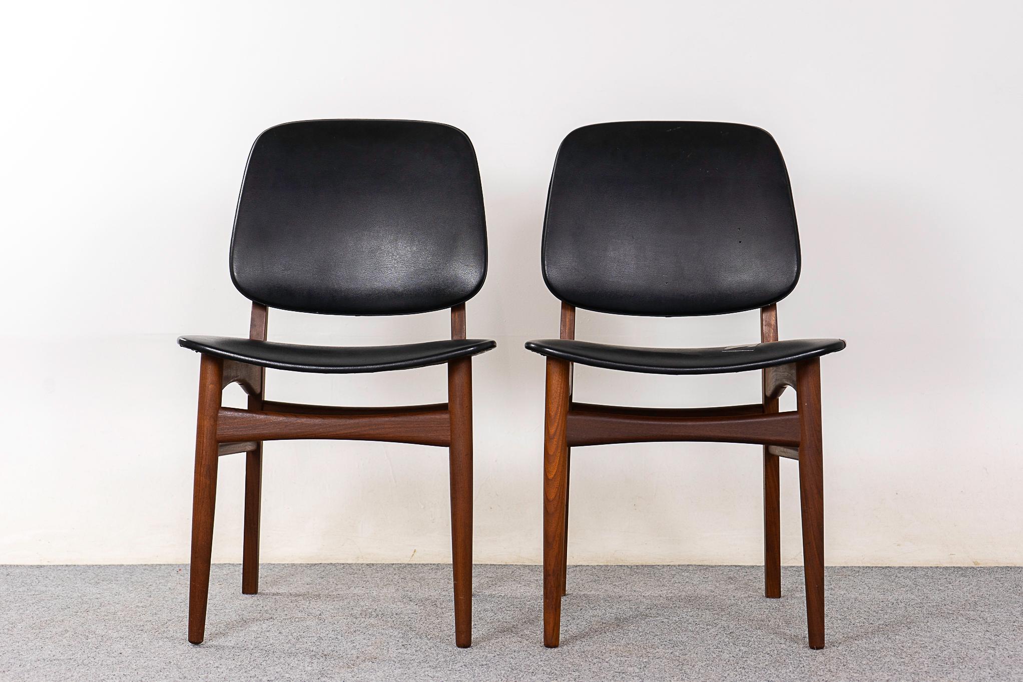 Teak Danish dining chair pair, circa 1960's. Elegant rich toned solid wood frames with bowtie cross supports and floating seats. Original jet black vinyl with wear/patch on 1 seat.