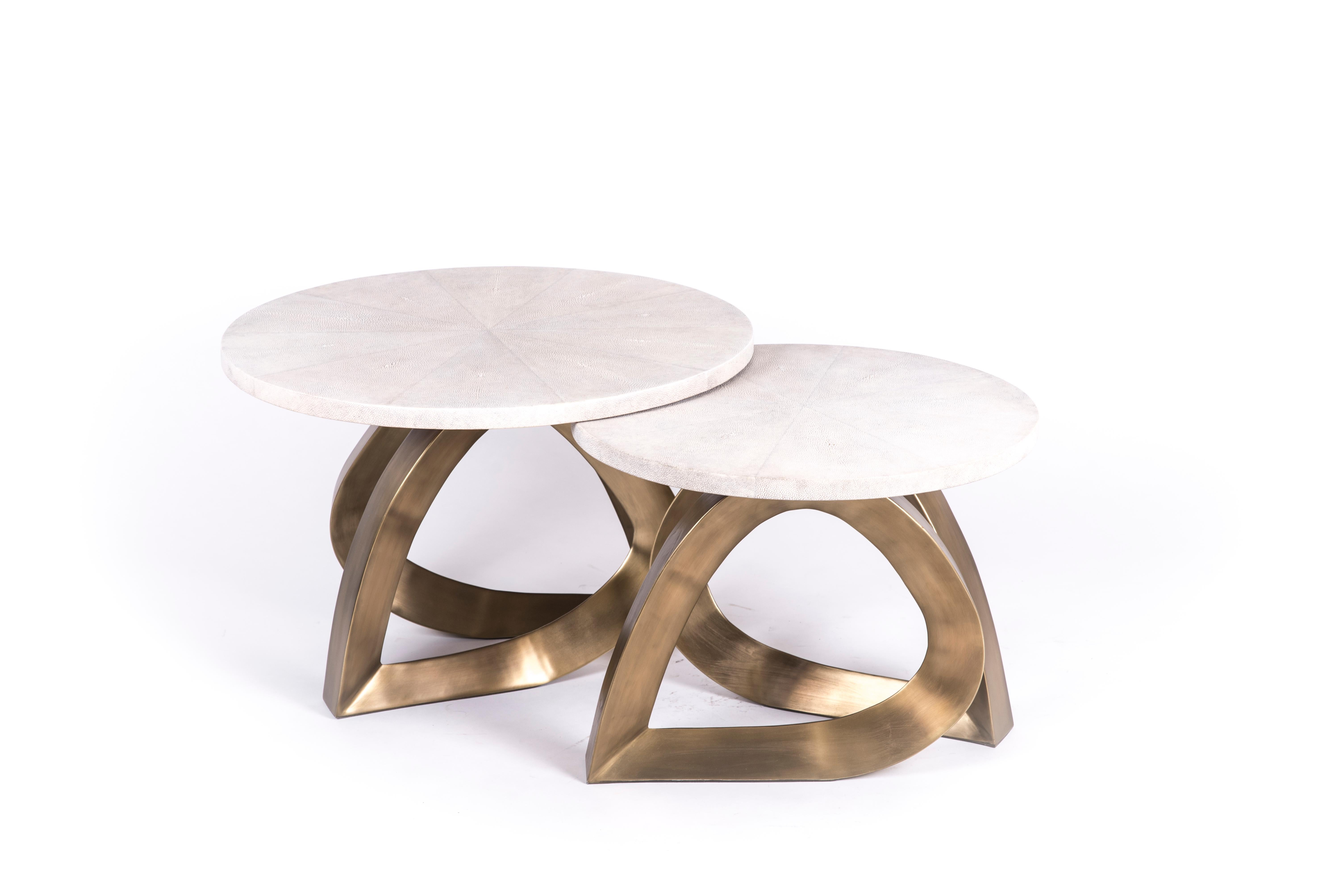 The set of 2 teardrop nesting coffee tables in cream shagreen and bronze-patina is an elegant design with circular top that sits on a sculptural base. The sculptural base is inlaid in bronze-patina brass and the top is in cream shagreen. These
