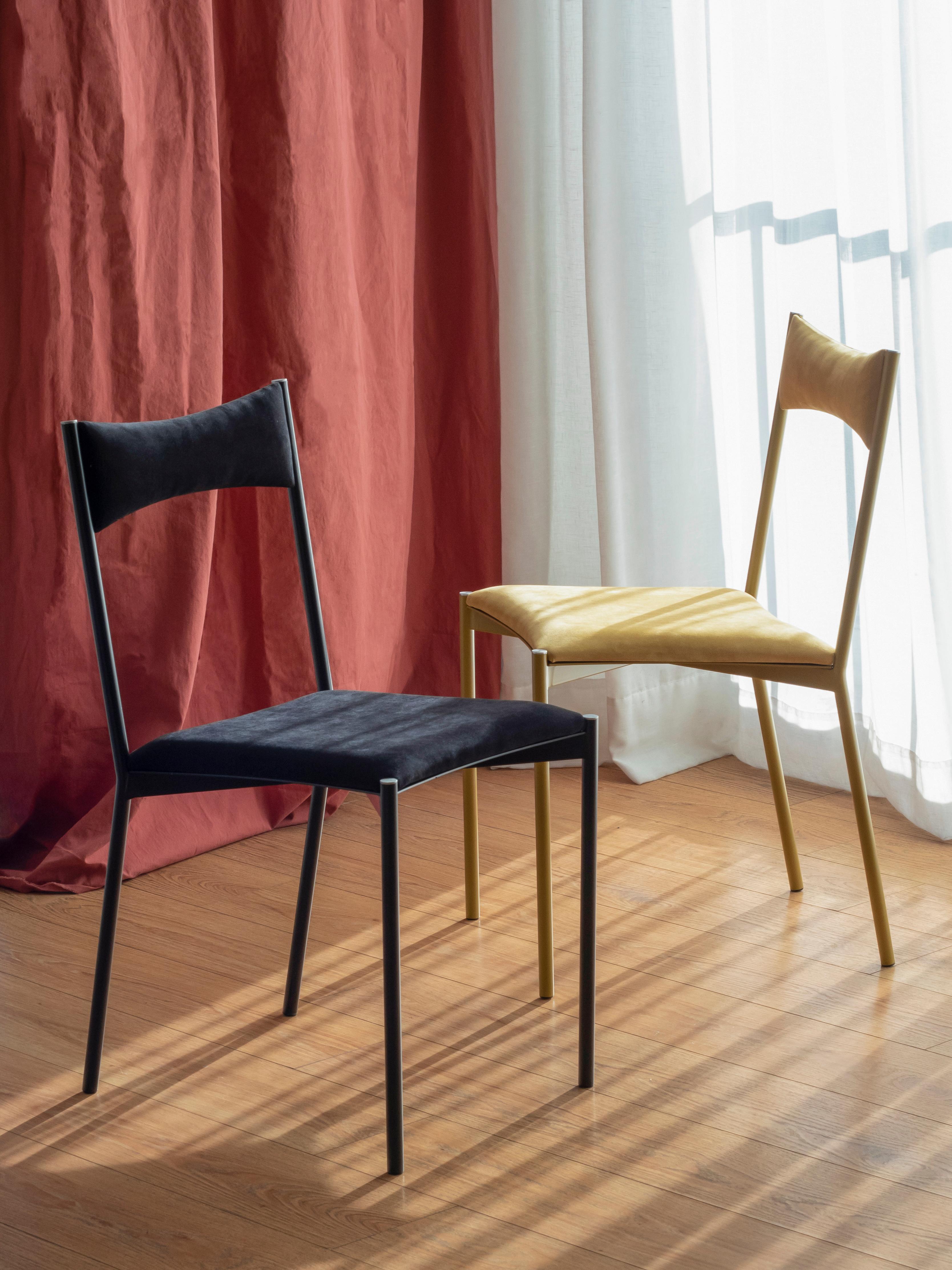 Un set di 2 sedie tensa, gialle e nere, di Ries
Dimensioni: L 40 x P 49,5 x H 82 cm 
Materiali: Tubo d'acciaio rotondo, lamiera tagliata al laser, schiuma ad alta densità, imbottitura in velluto, tappi in alluminio/bronzo
Verniciatura a polvere
