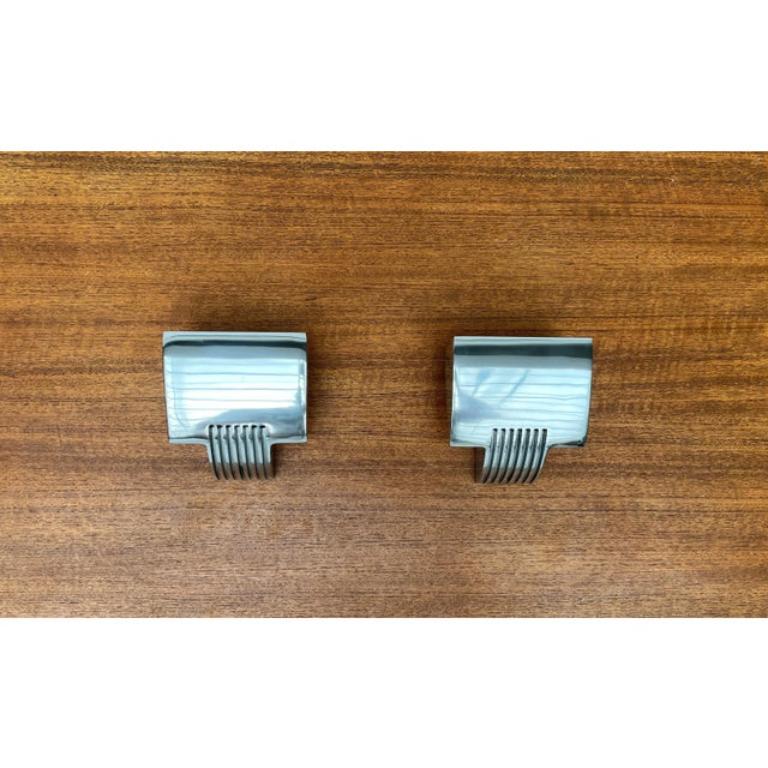Two elegant wall lights from the Spanish manufacturer Metalarte.

The heavy lamp body is made of cast aluminum, which gives the lamp a monolithic appearance. The surface is polished to a shine. The ribs in the lower area, which seem to merge into