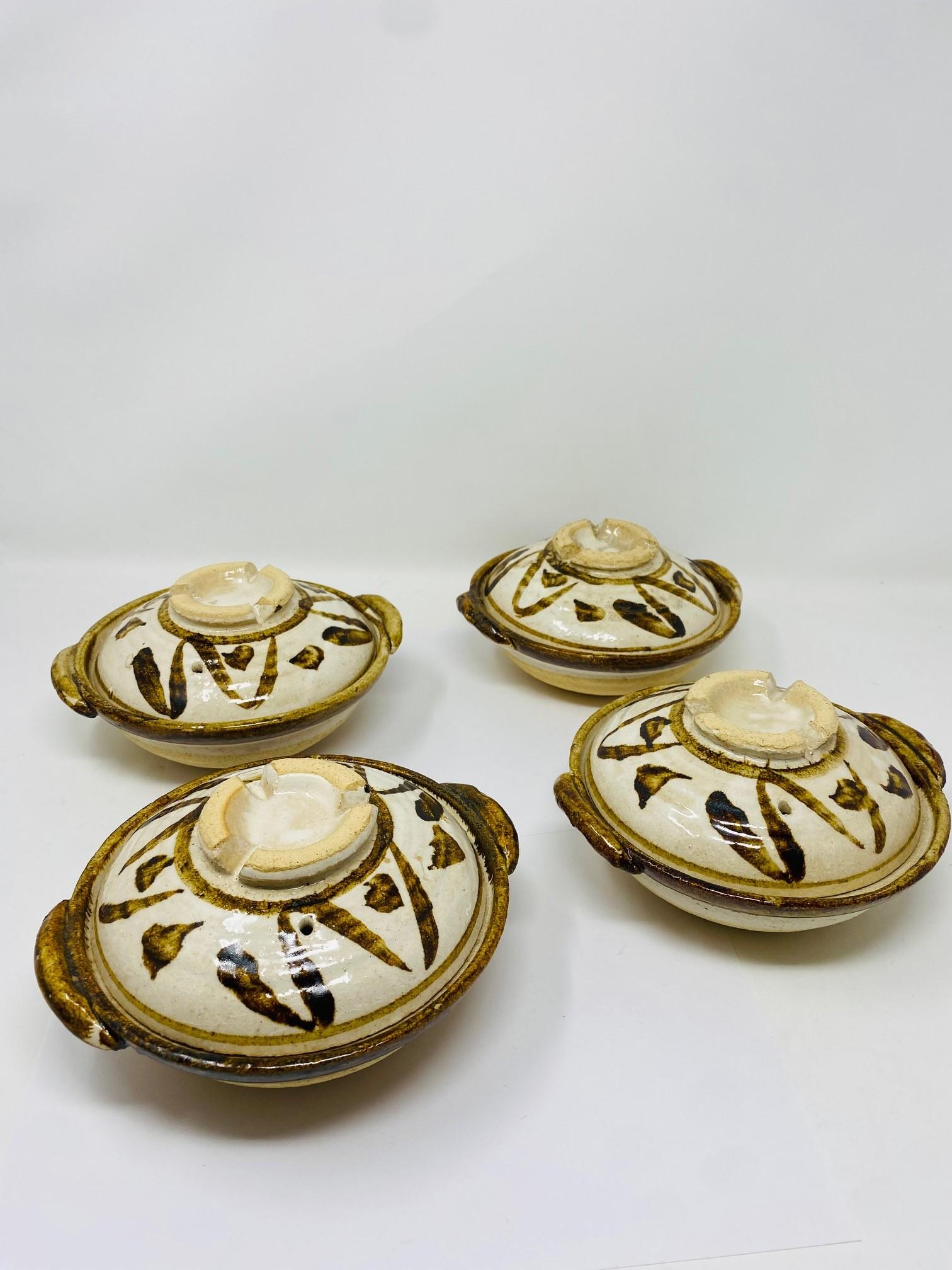 Beautiful set of 2 vintage studio pottery covered bowls.  These handcrafted dishes feature vented lids and shoulder handles. A hand painted abstract design accents the natural beige glazed pottery with dark brown accents.  Beautifully rustic yet