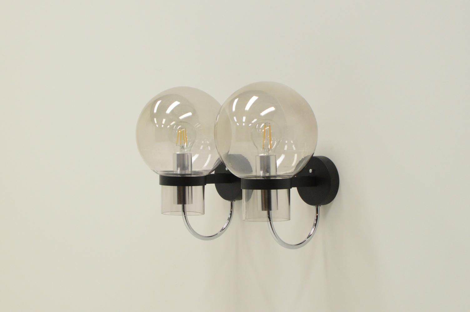 Ensemble de 2 lampes murales de Glashütte Limburg, années 1960, Allemagne. Support mural en métal noir mat et globe en verre légèrement teinté. Contient une ampoule E27. Les supports muraux sont remis à neuf. Légères rayures sur les globes en verre.